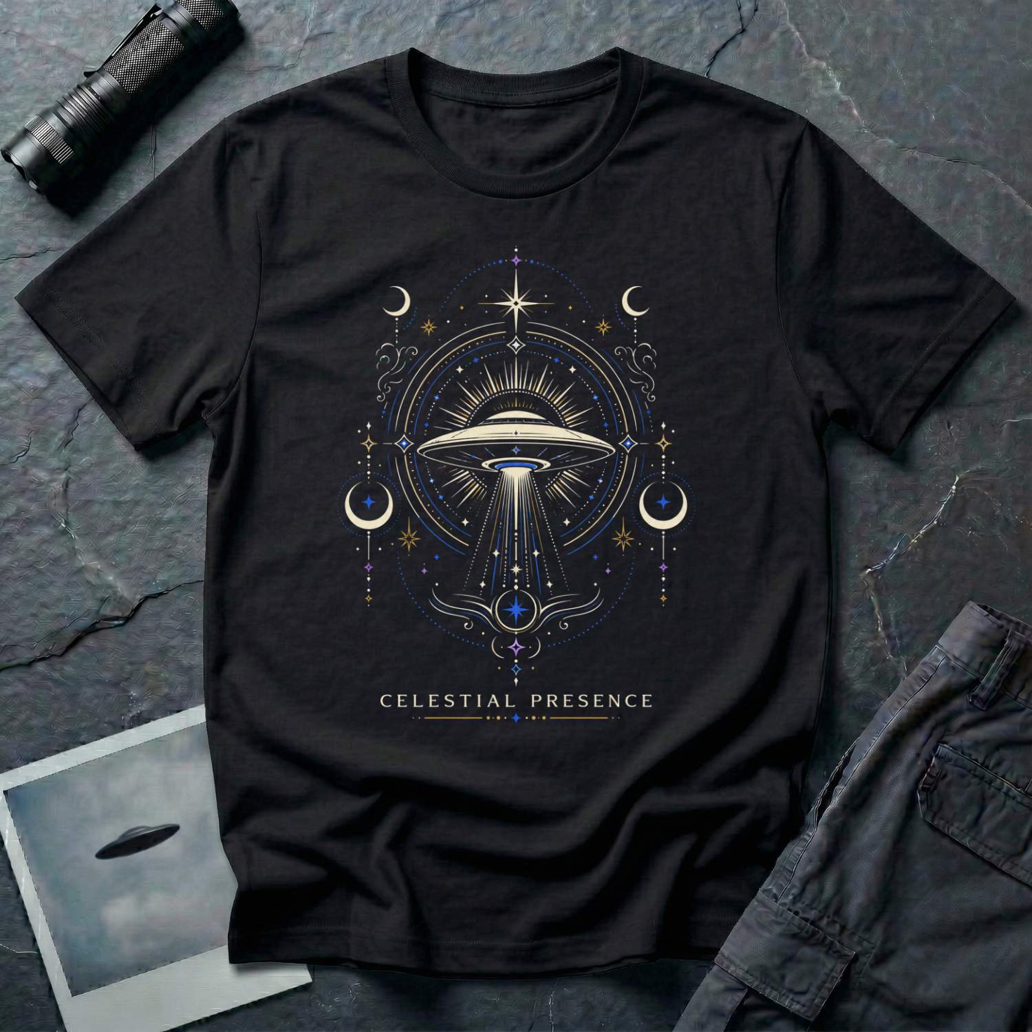 Black t-shirt with a symmetrical celestial UFO illustration featuring crescent moons, four-pointed stars and ornate scrollwork framing a central saucer in gold and blue linework with CELESTIAL PRESENCE caption