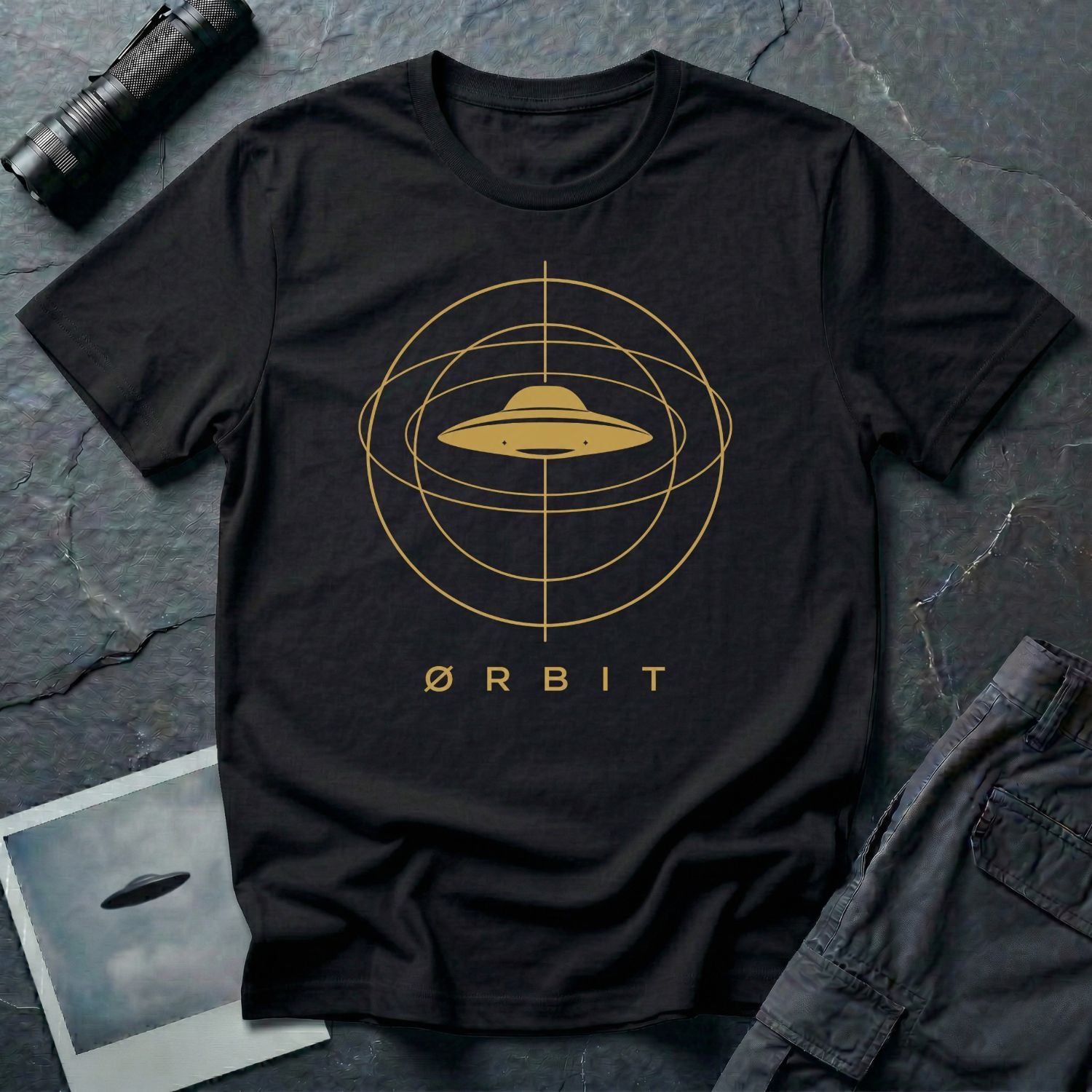 Orbit astronomical UFO t-shirt — flying saucer centred in a gold orbital sphere framework with "Ørbit" sans serif typography on black cotton tee