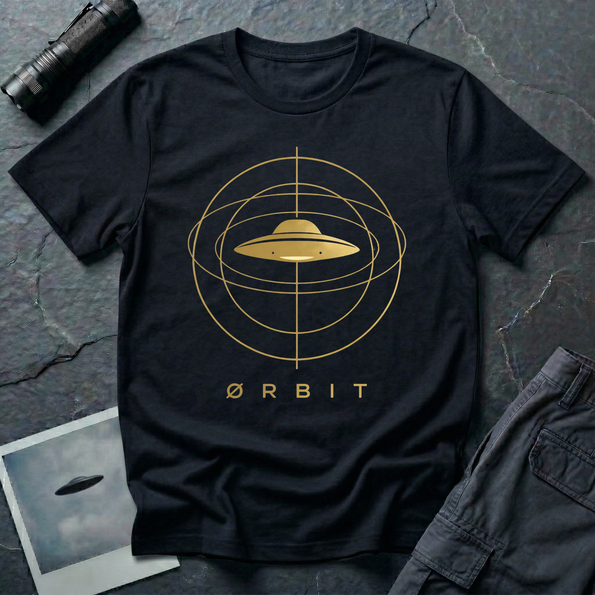 Orbit astronomical UFO t-shirt — flying saucer centred in a gold orbital sphere framework with "Ørbit" sans serif typography on black cotton tee