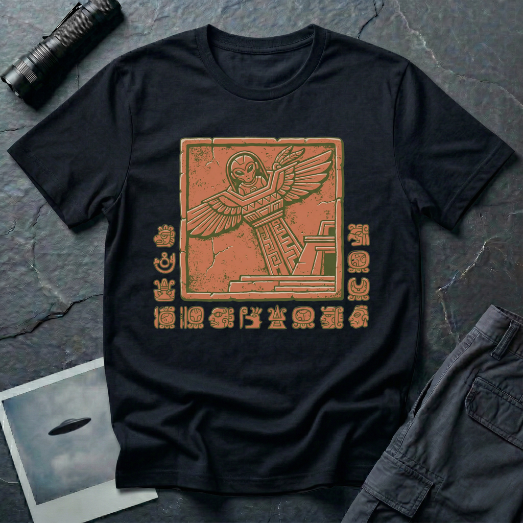 Aztec alien t-shirt — ancient astronaut figure with grey alien head in Mesoamerican feathered dress on stepped pyramid. Weathered stone relief on black cotton tee.
