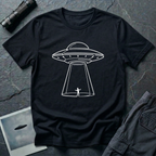 One Line UFO minimalist line art t-shirt — hand-drawn flying saucer beaming down over a tiny stick figure in one continuous white line on black cotton tee