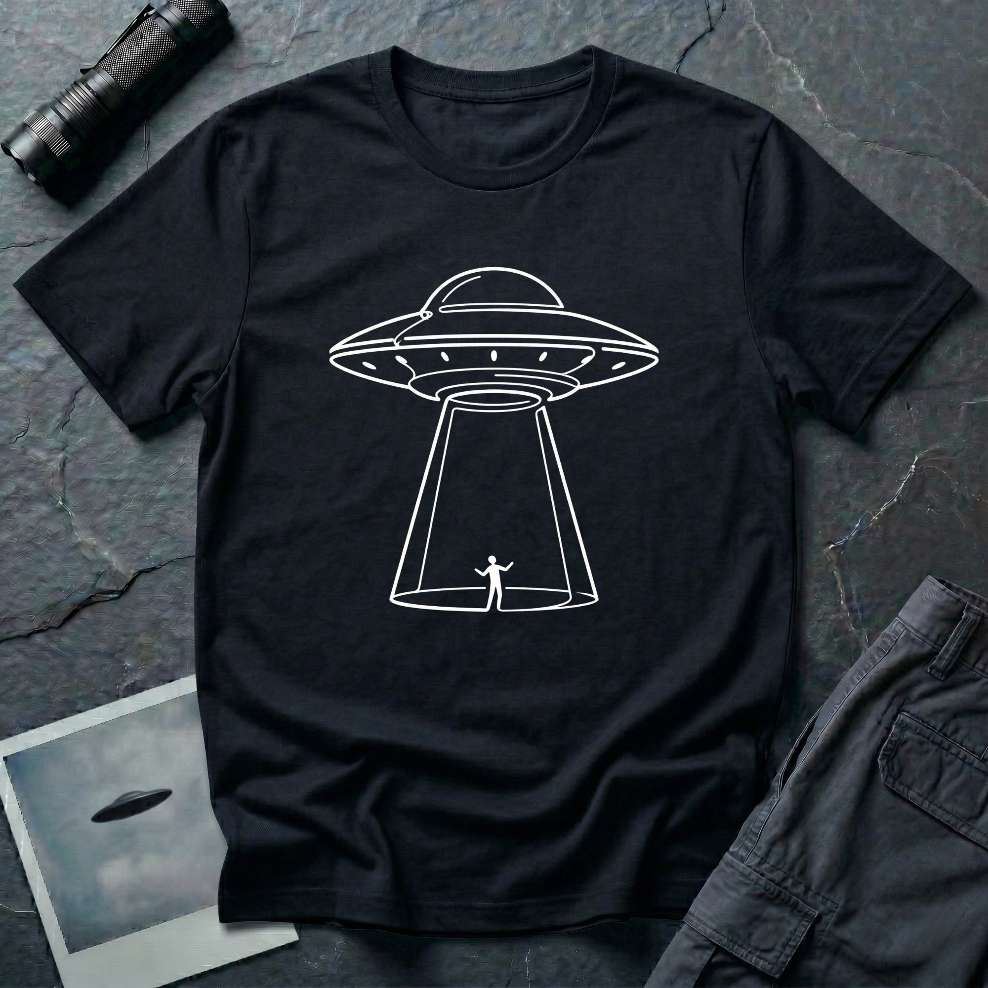 One Line UFO minimalist line art t-shirt — hand-drawn flying saucer beaming down over a tiny stick figure in one continuous white line on black cotton tee