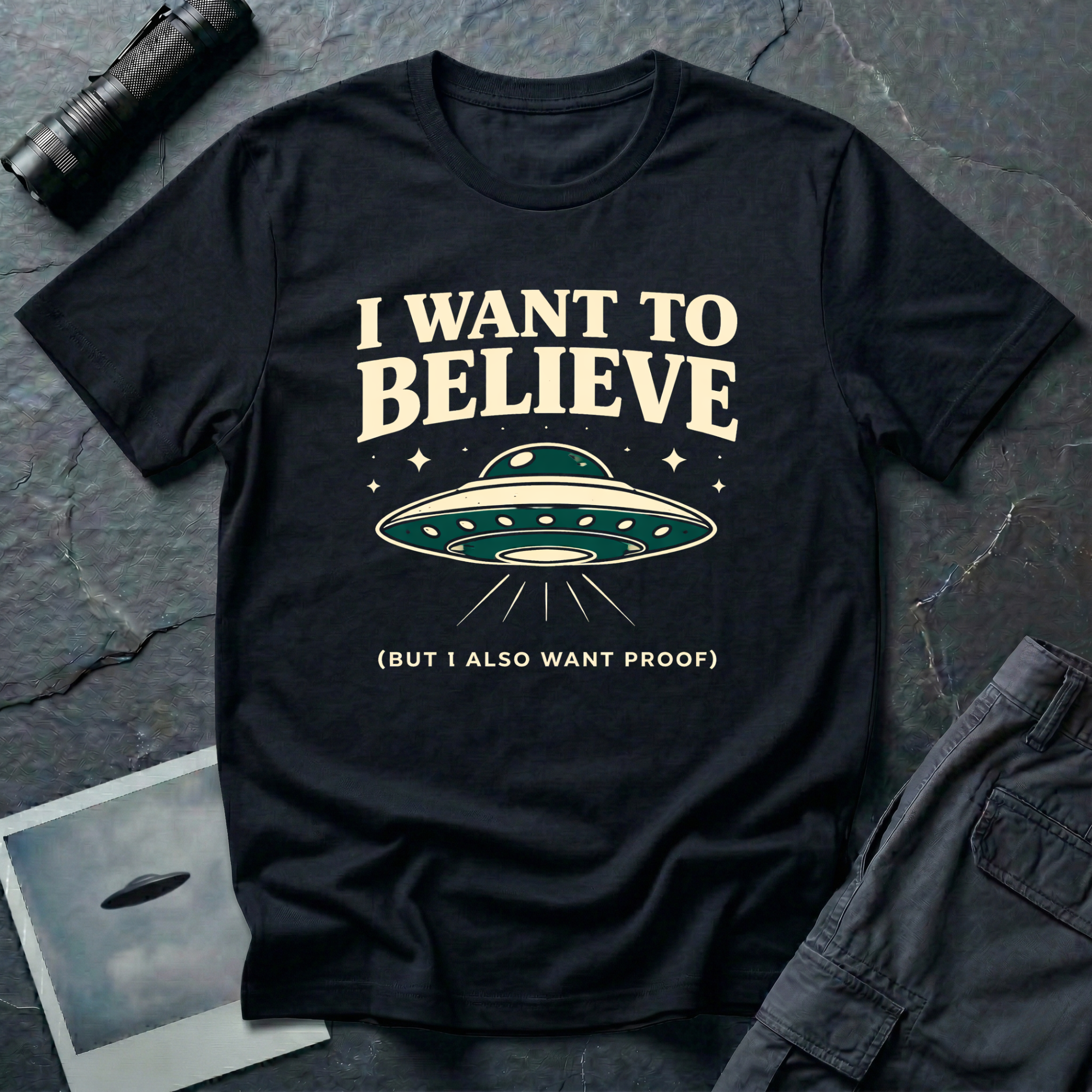 I Want To Believe ironic UFO t-shirt — classic teal saucer with the phrase "I want to believe (but I also want proof)" on black cotton tee