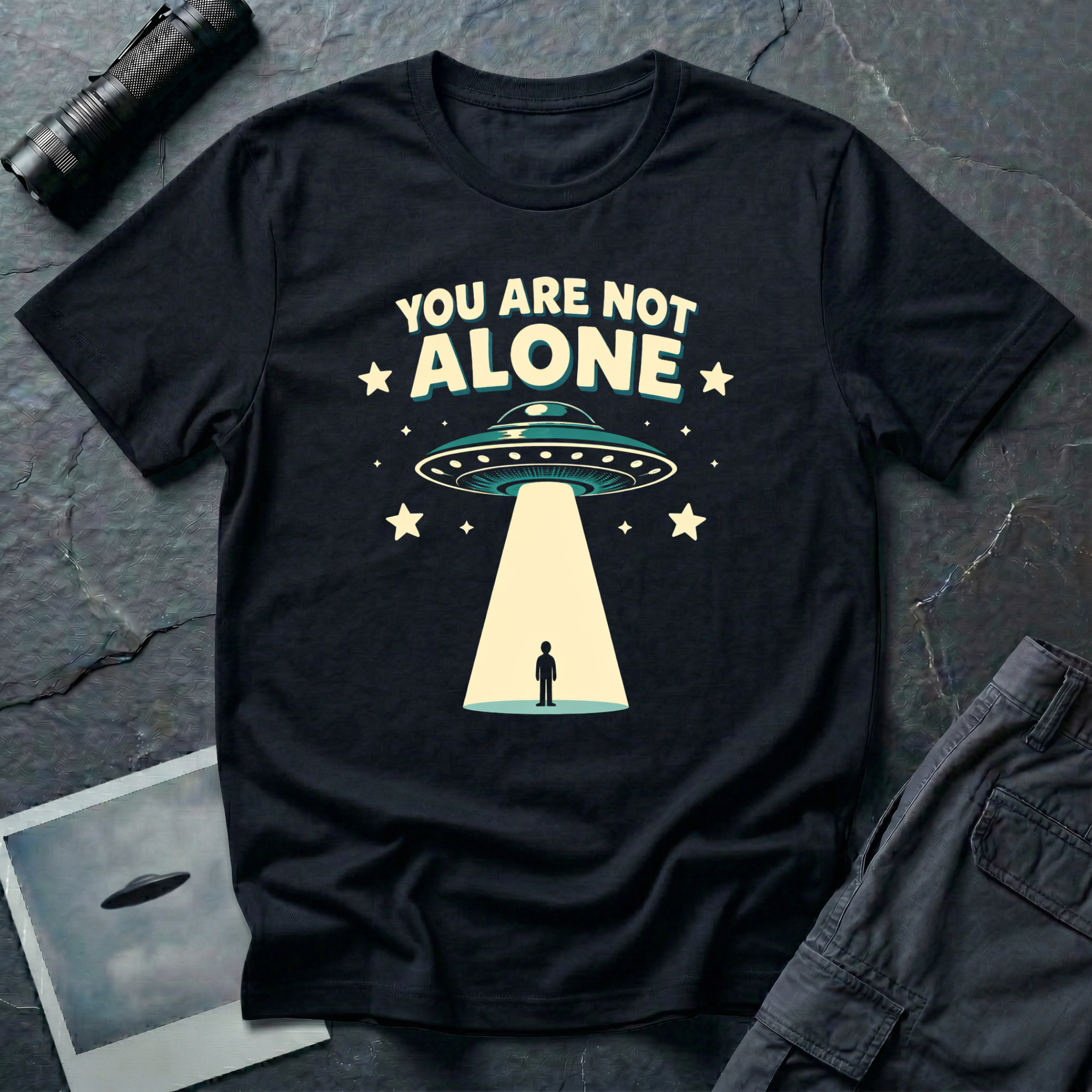 You Are Not Alone friendly UFO t-shirt — retro saucer beaming down on a calm human figure with "You Are Not Alone" text on black cotton tee