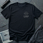 UAP logo t-shirt — small minimalist saucer icon and UAP letters in grey on the upper left chest of black cotton tee