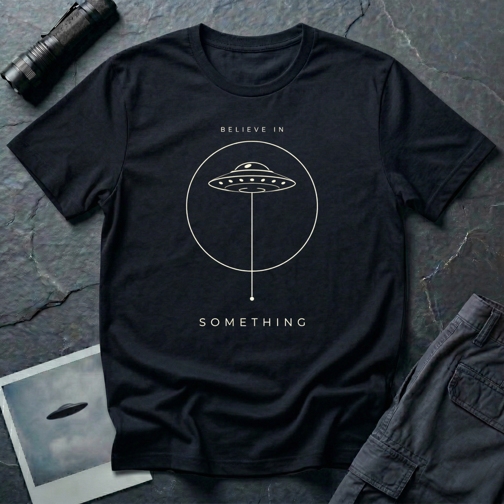 Believe in Something minimalist UFO t-shirt — flying saucer inside a circle with a suspended plumb line in cream on black cotton tee