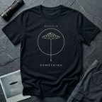 Believe in Something minimalist UFO t-shirt — flying saucer inside a circle with a suspended plumb line in cream on black cotton tee