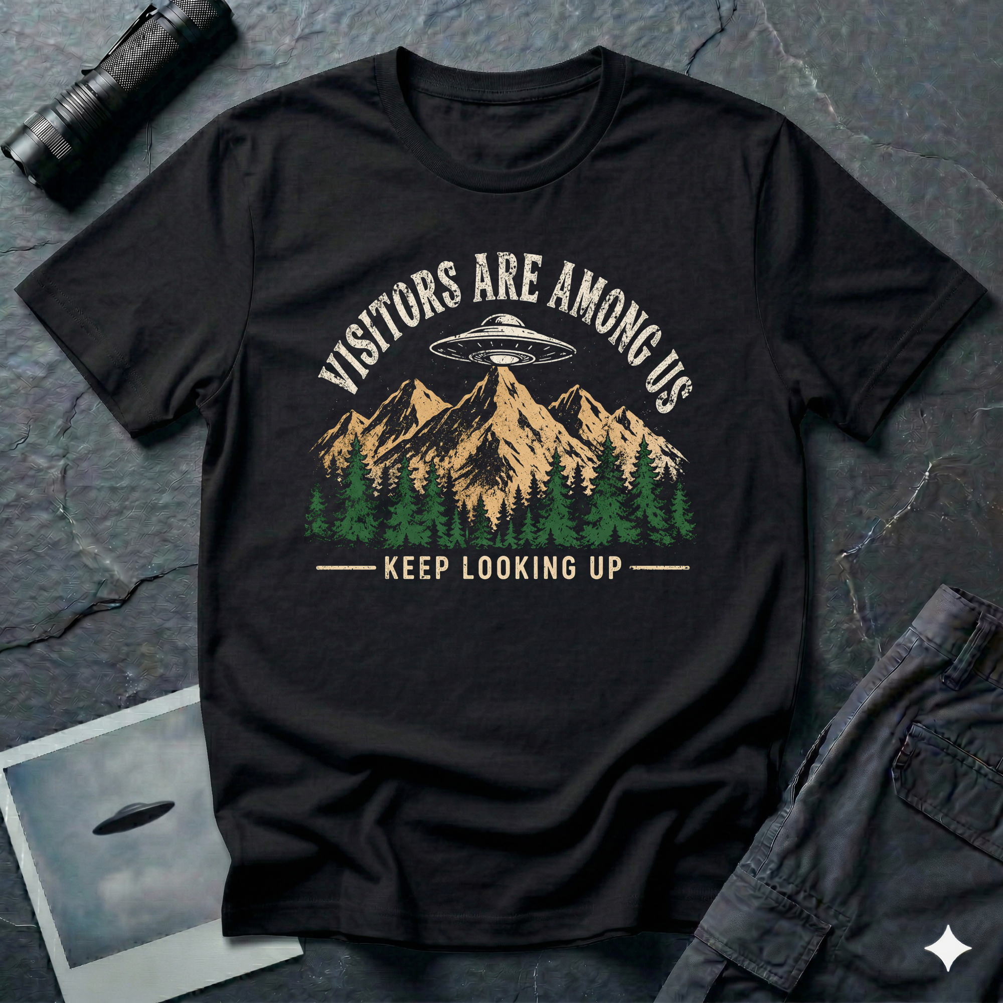 Visitors Are Among Us outdoor UFO t-shirt — flying saucer over mountain range and pine forest on black unisex cotton tee