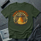 Visit Roswell UFO t-shirt — vintage circular tourism badge with flying saucer beaming over desert cacti in rust and mustard tones on green cotton tee