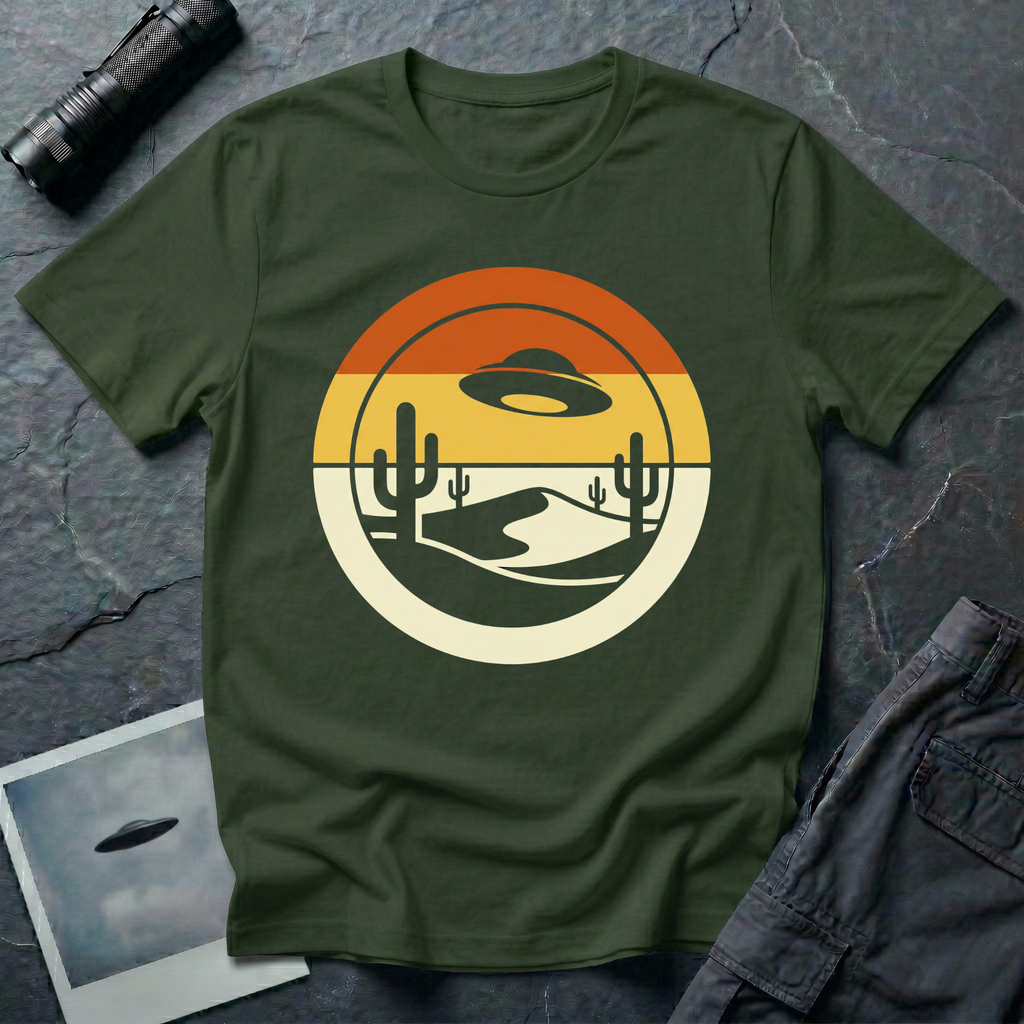 Desert Sun sunset UFO t-shirt — classic flying saucer silhouette over layered retro sunset sky with burnt orange and warm yellow bands, two saguaro cacti and a cream desert dune in a clean circular graphic composition on dark green cotton tee
