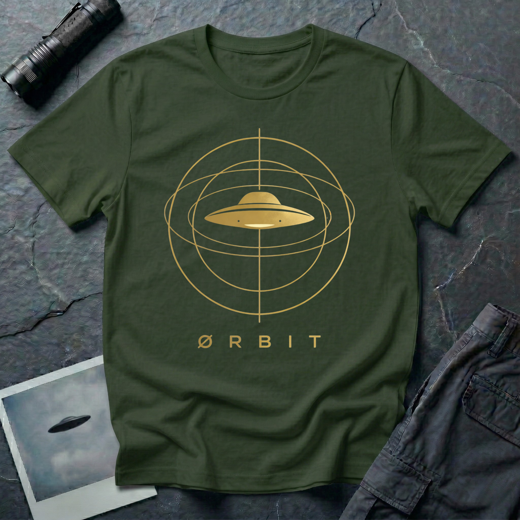 Orbit astronomical UFO t-shirt — flying saucer centred in a gold orbital sphere framework with "Ørbit" sans serif typography on green cotton tee