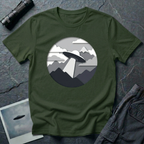Papercut UFO t-shirt — layered paper-craft illustration of flying saucer over mountains and clouds in grey monochrome on green cotton tee