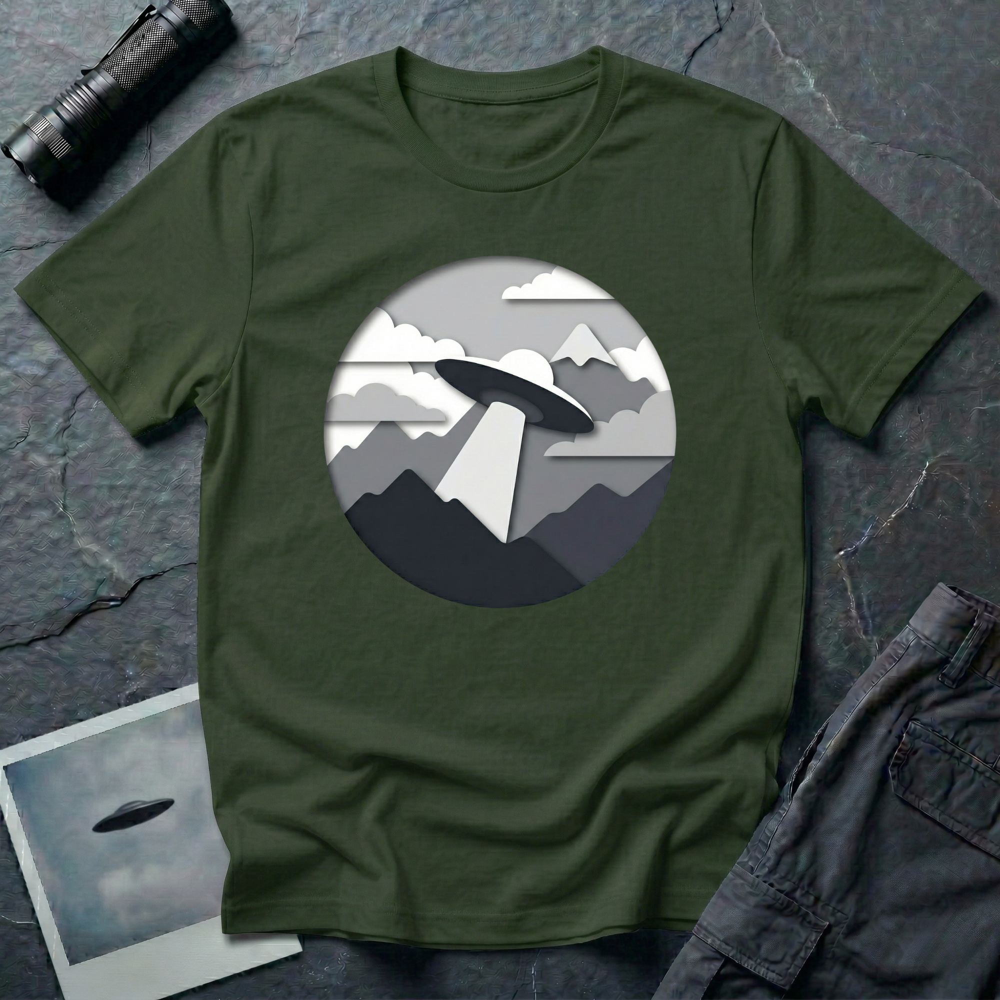 Papercut UFO t-shirt — layered paper-craft illustration of flying saucer over mountains and clouds in grey monochrome on green cotton tee