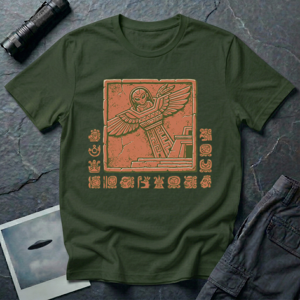 Aztec alien t-shirt — ancient astronaut figure with grey alien head in Mesoamerican feathered dress on stepped pyramid. Weathered stone relief on green cotton tee.