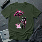 Out of This Town stencil UFO t-shirt — astronaut holding flying saucer like a balloon in Banksy-style street art with hot pink accents on military green cotton tee