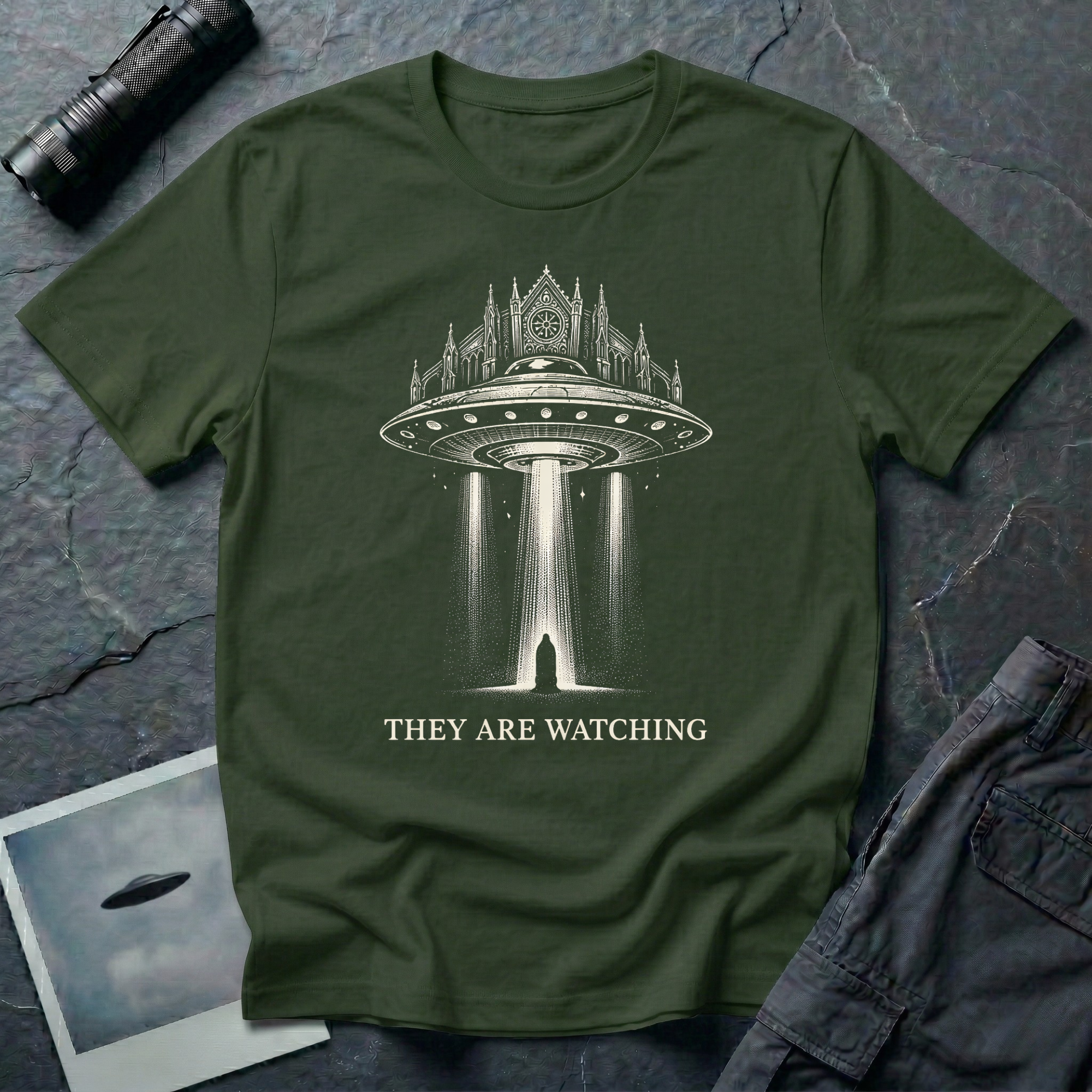 They Are Watching Gothic UFO t-shirt — medieval cathedral fused with flying saucer beaming down on hooded figure in cream line-work on military green cotton tee