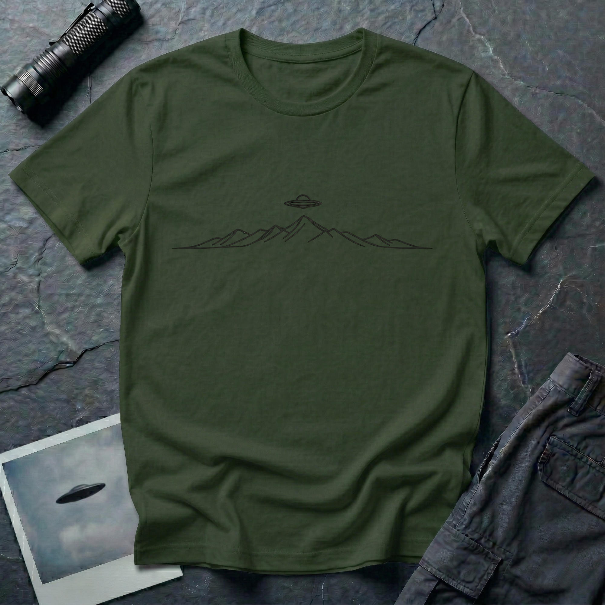Line Drawing UFO minimalist mountain t-shirt — fine black linework mountain range with small flying saucer above the central peak on green cotton tee