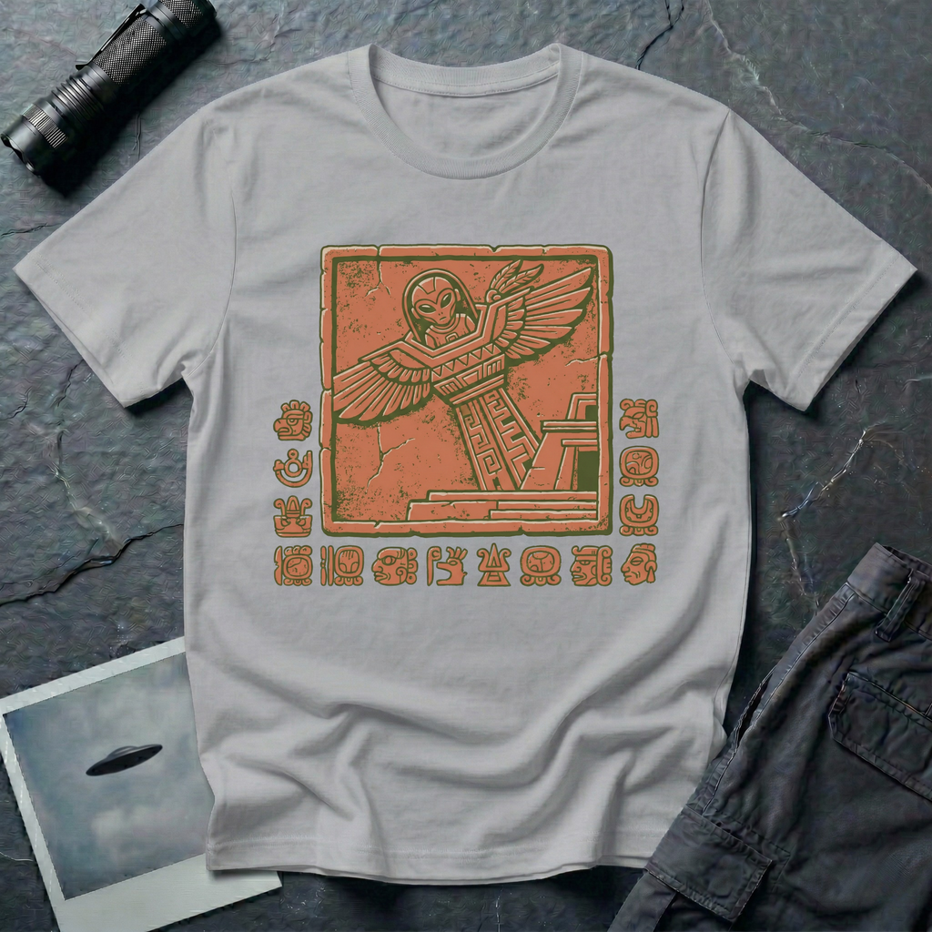 Aztec alien t-shirt — ancient astronaut figure with grey alien head in Mesoamerican feathered dress on stepped pyramid. Weathered stone relief on grey cotton tee.