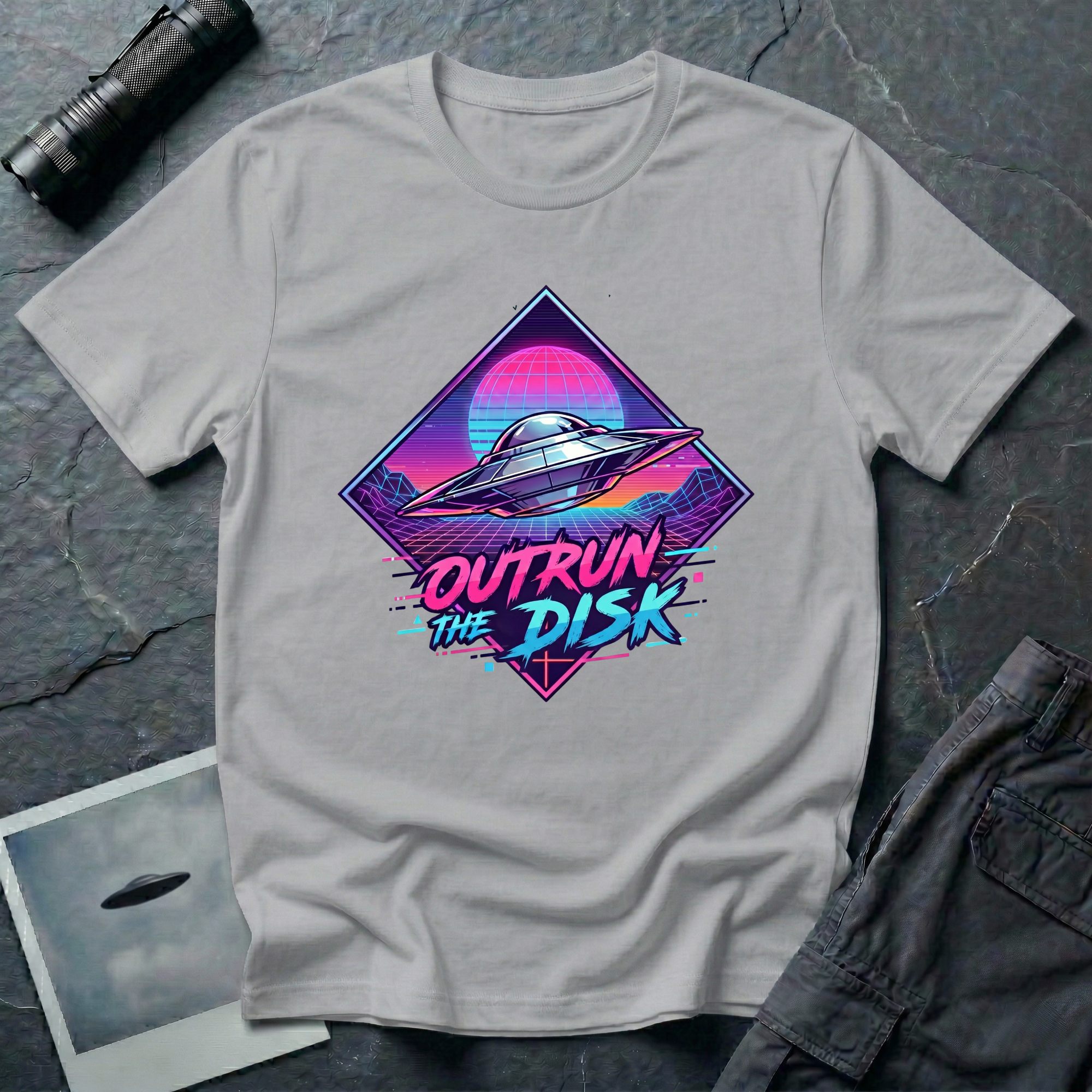 Outrun The Disk synthwave UFO t-shirt — chrome saucer across neon grid landscape with wireframe sun and retrowave typography on grey cotton tee