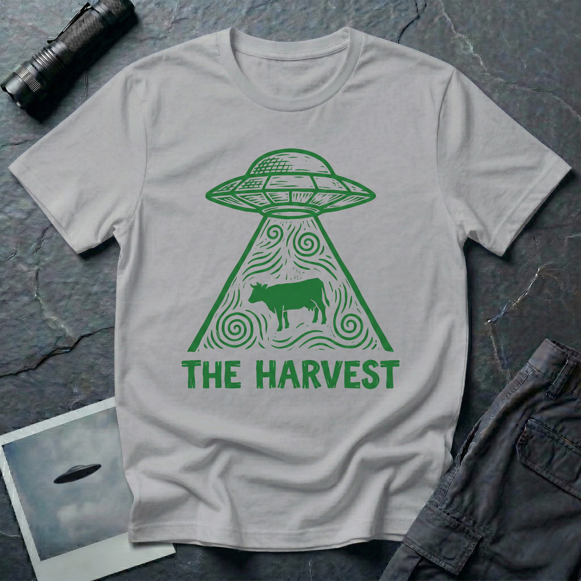 The Harvest dark folklore UFO t-shirt — linocut flying saucer with swirling beam abducting a lone cow in green on grey cotton tee