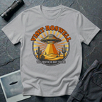 Visit Roswell UFO t-shirt — vintage circular tourism badge with flying saucer beaming over desert cacti in rust and mustard tones on grey cotton tee