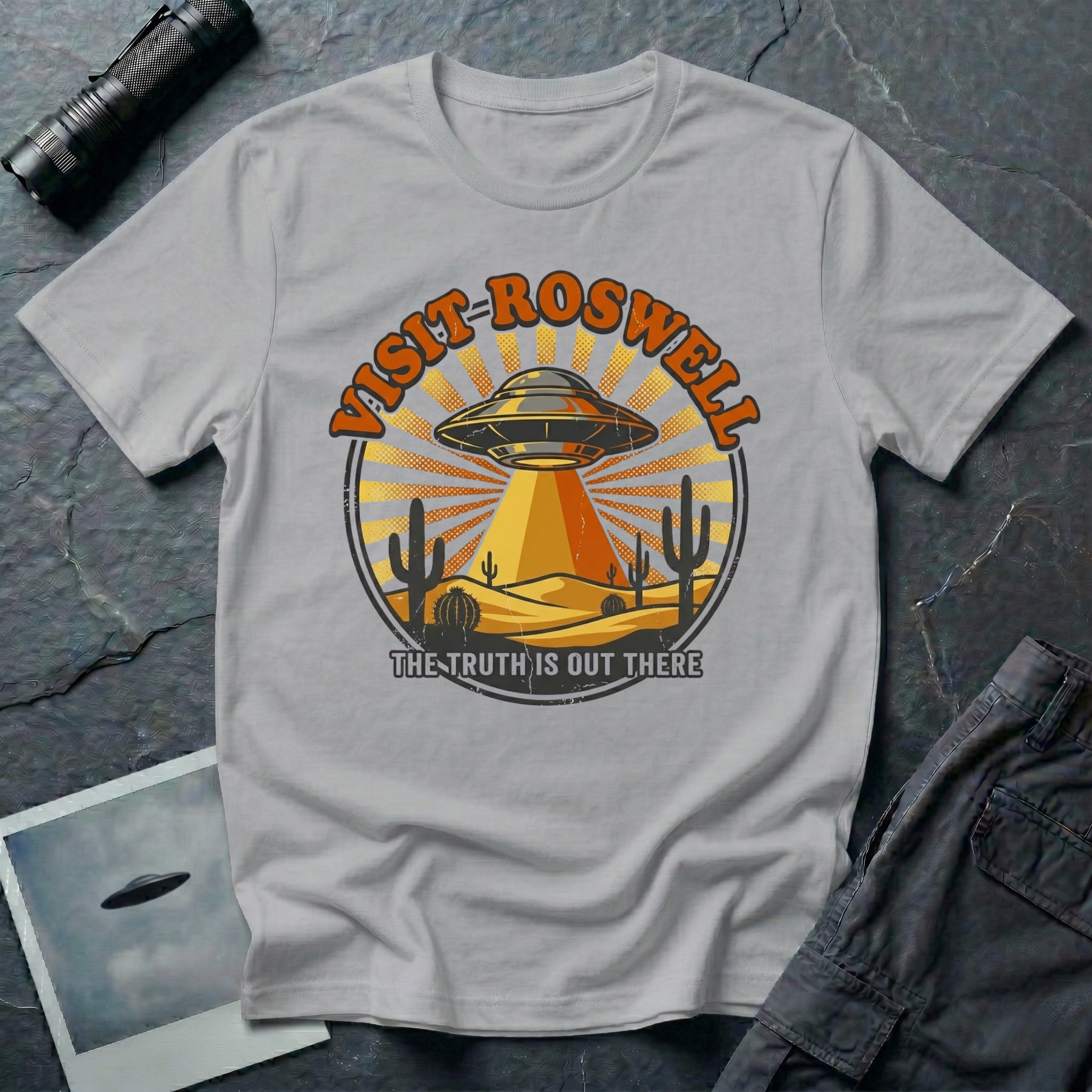 Visit Roswell UFO t-shirt — vintage circular tourism badge with flying saucer beaming over desert cacti in rust and mustard tones on grey cotton tee