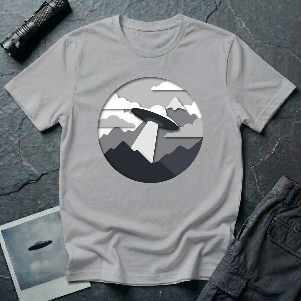 Papercut UFO t-shirt — layered paper-craft illustration of flying saucer over mountains and clouds in grey monochrome on grey cotton tee