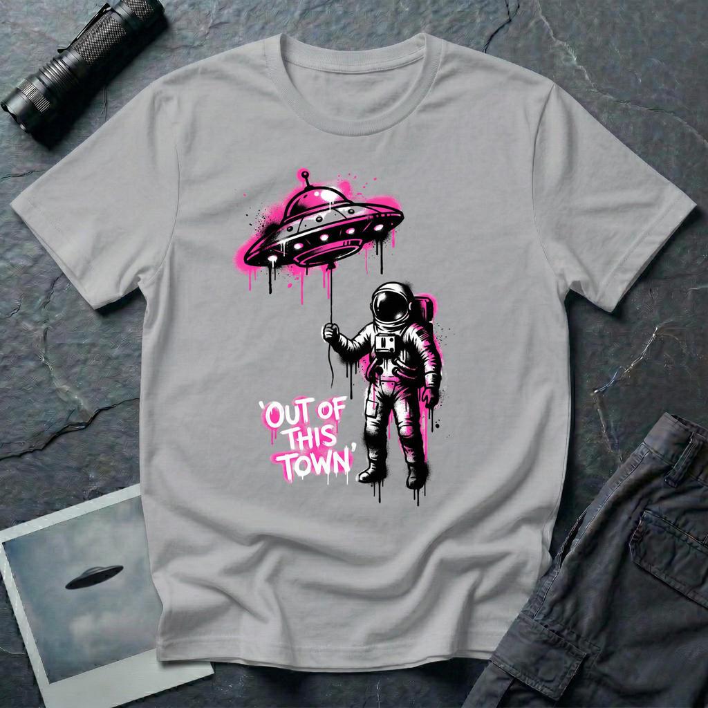 Out of This Town stencil UFO t-shirt — astronaut holding flying saucer like a balloon in Banksy-style street art with hot pink accents on grey cotton tee