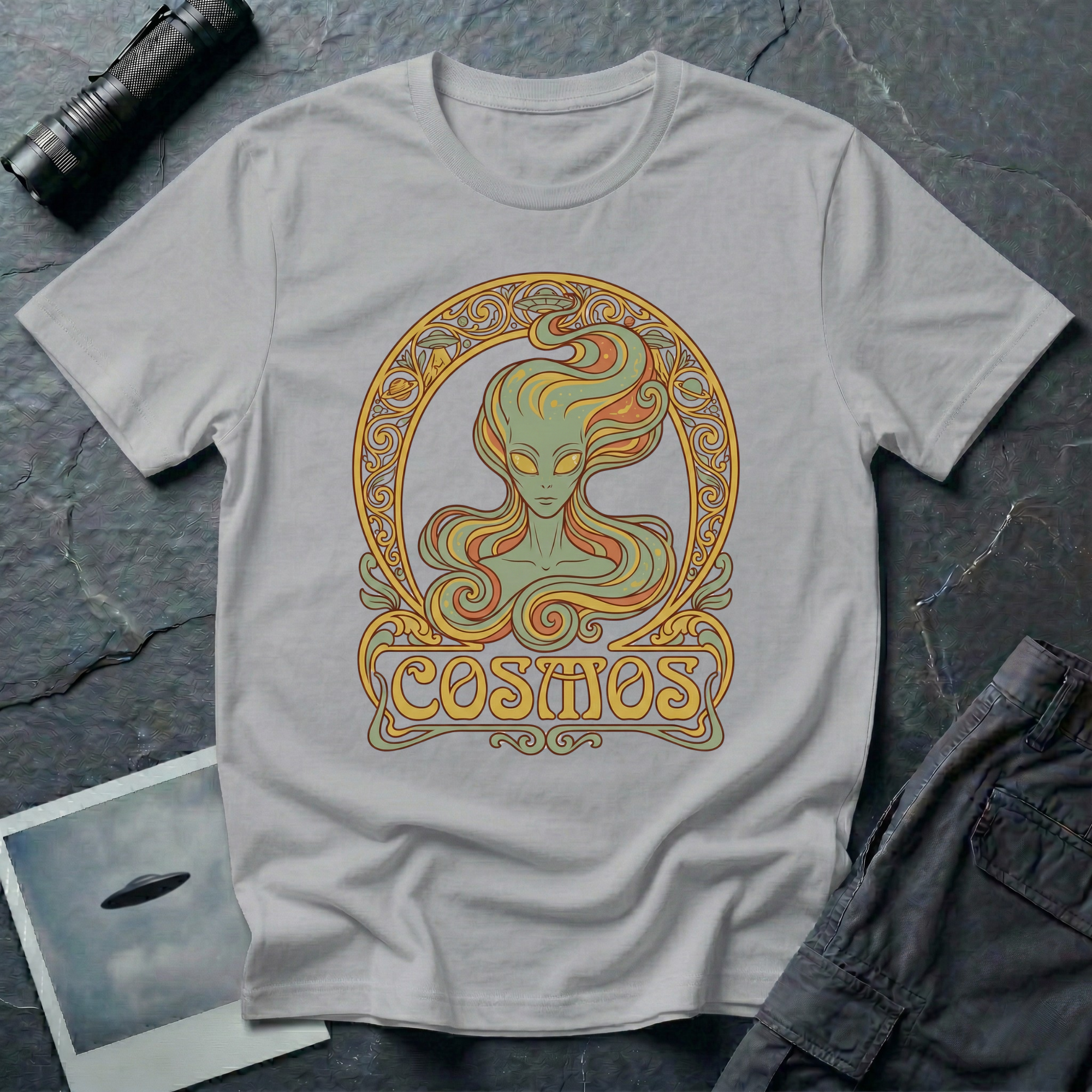 Cosmos Art Nouveau alien t-shirt — green grey alien portrait with large almond eyes and flowing orange hair in ornate gold decorative frame with scrollwork and "Cosmos" banner on grey cotton tee