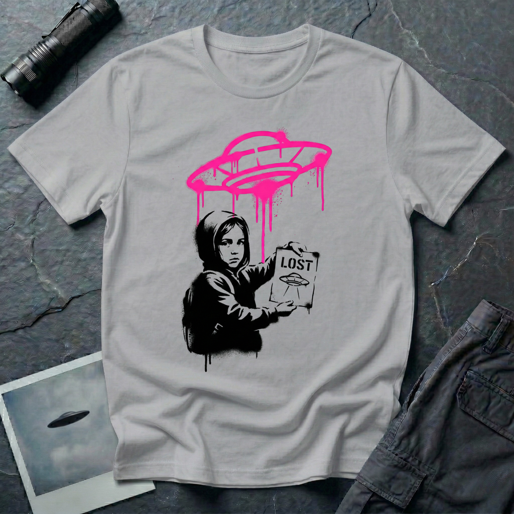 Street art UFO t-shirt with black stencil hooded figure holding "LOST" poster featuring flying saucer icon, bright magenta spray-painted UFO with paint drips hovering above in Banksy graffiti style on grey cotton tee