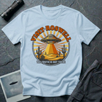 Visit Roswell UFO t-shirt — vintage circular tourism badge with flying saucer beaming over desert cacti in rust and mustard tones on light blue cotton tee