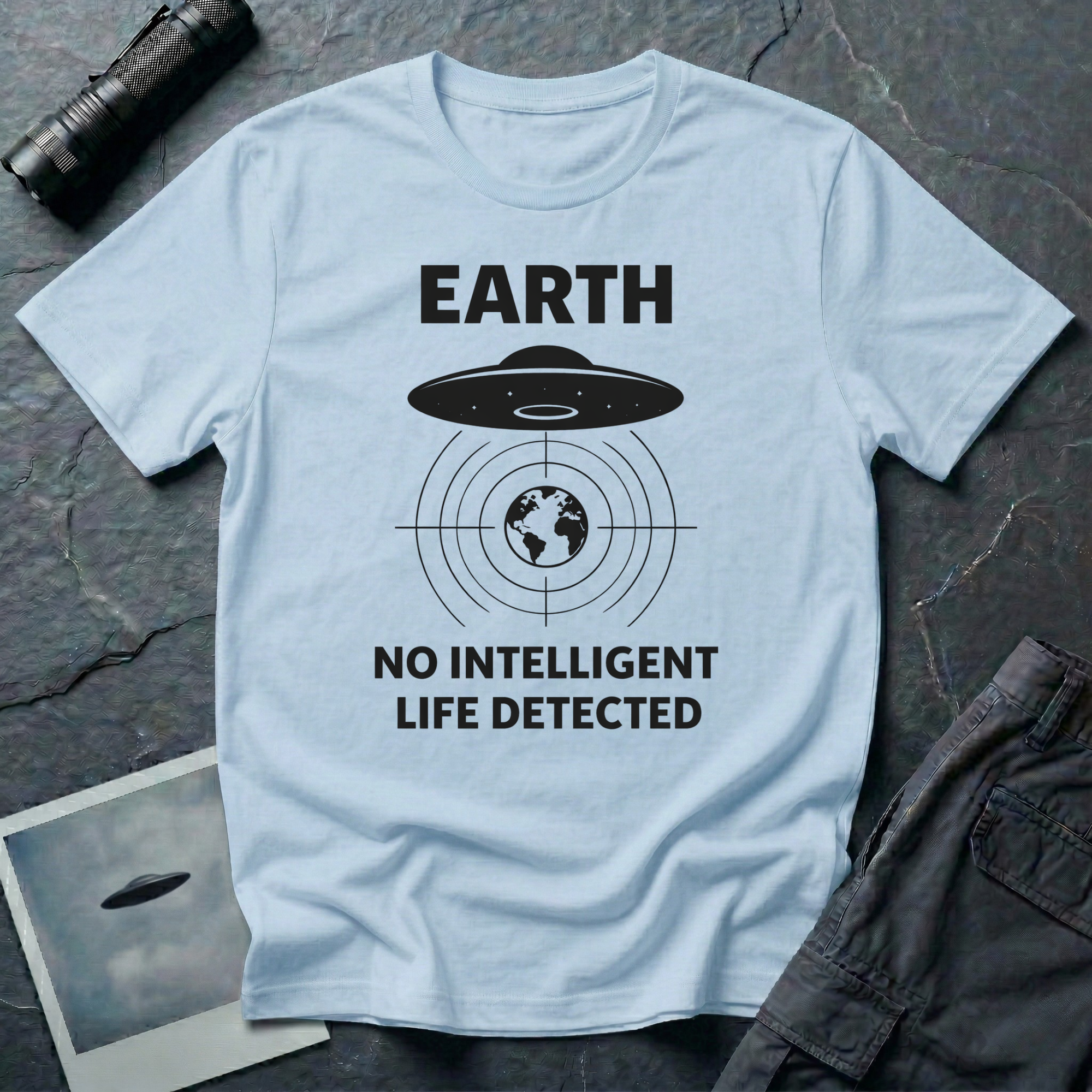 No Intelligent Life Detected UFO t-shirt — classic flying saucer above concentric scan rings and crosshairs targeting Earth with "EARTH / NO INTELLIGENT LIFE DETECTED" caption in black on light blue cotton tee