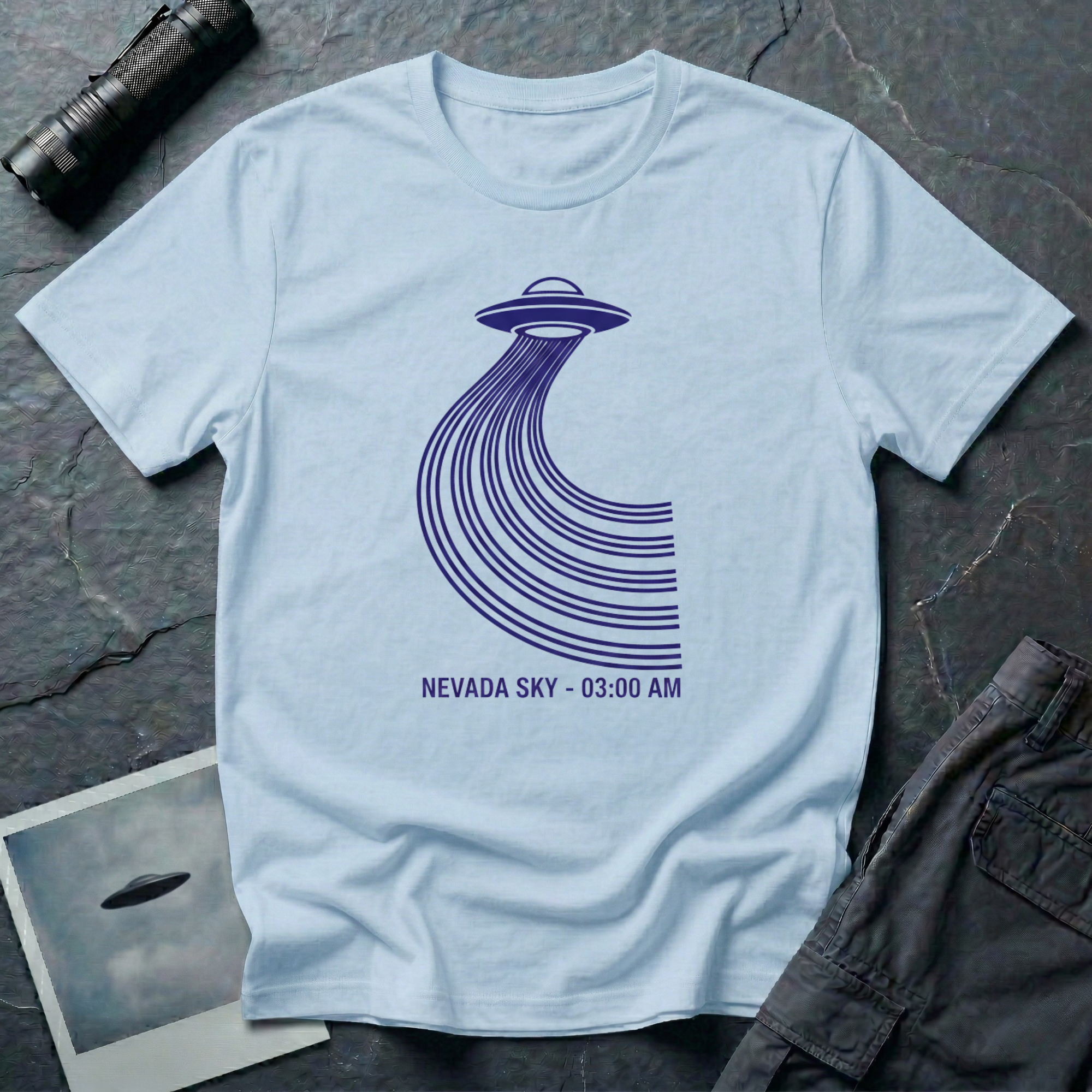 Nevada Sky 03:00 AM UFO sighting t-shirt — navy flying saucer with parabolic trail of parallel lines and timestamp caption on light blue cotton tee
