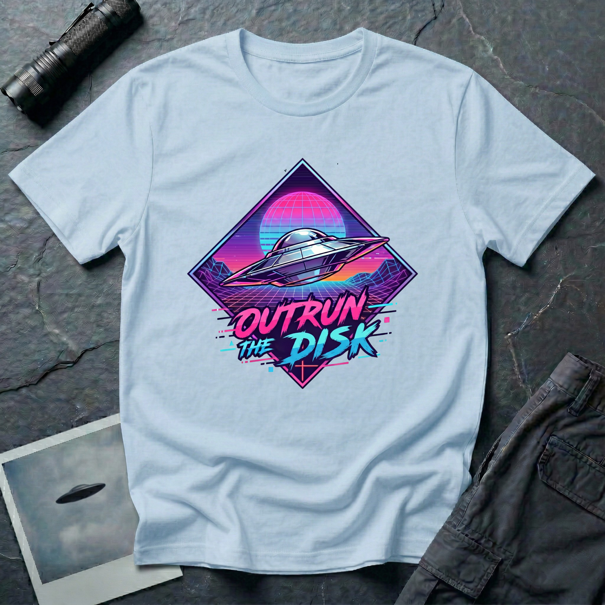 Outrun The Disk synthwave UFO t-shirt — chrome saucer across neon grid landscape with wireframe sun and retrowave typography on light blue cotton tee
