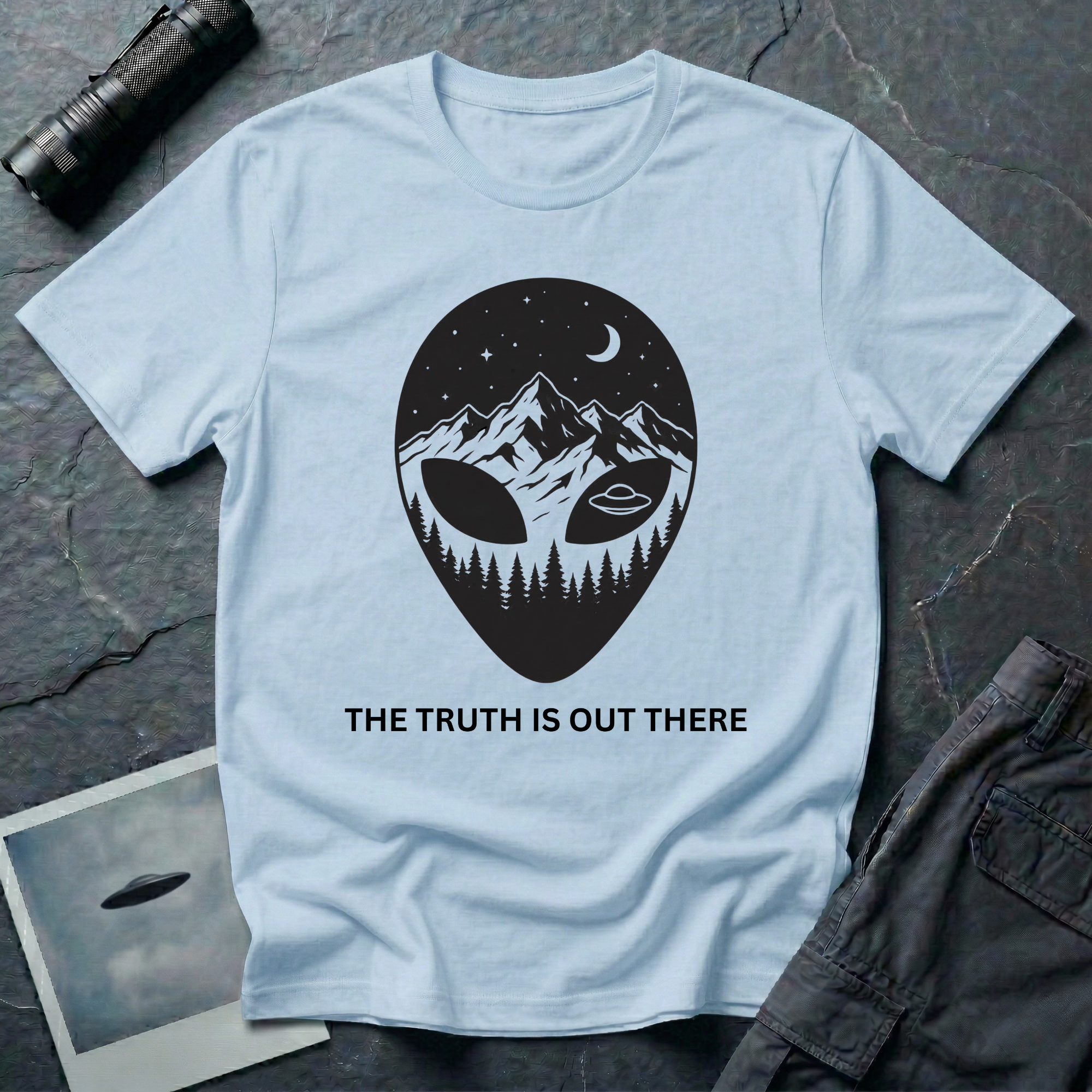 The Truth Is Out There alien head t-shirt — alien silhouette filled with mountains, pine forest and flying saucer on light blue cotton tee