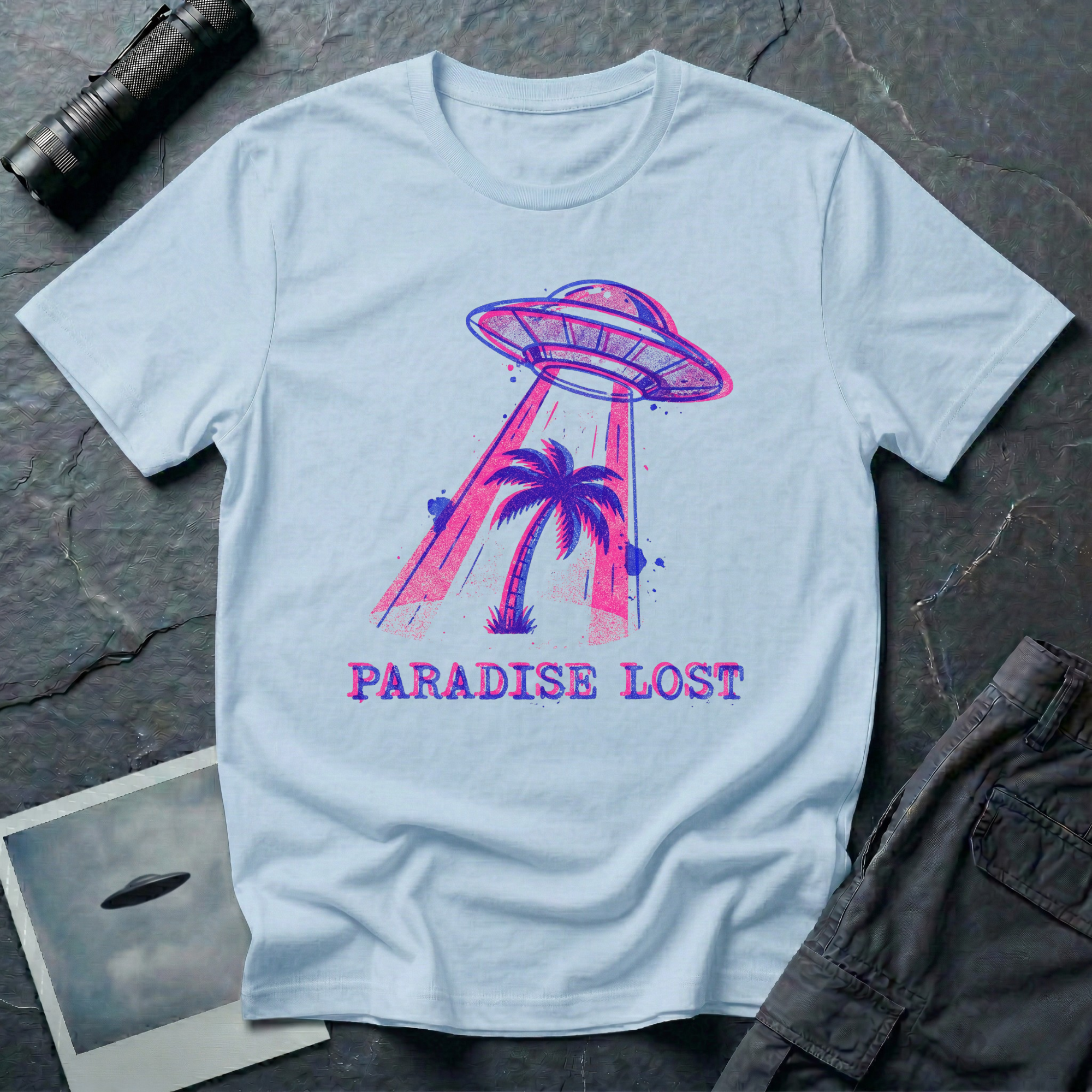 Paradise Lost tropical UFO t-shirt — palm tree being lifted into flying saucer tractor beam in pink and blue riso print with "Paradise Lost" caption on light blue cotton tee