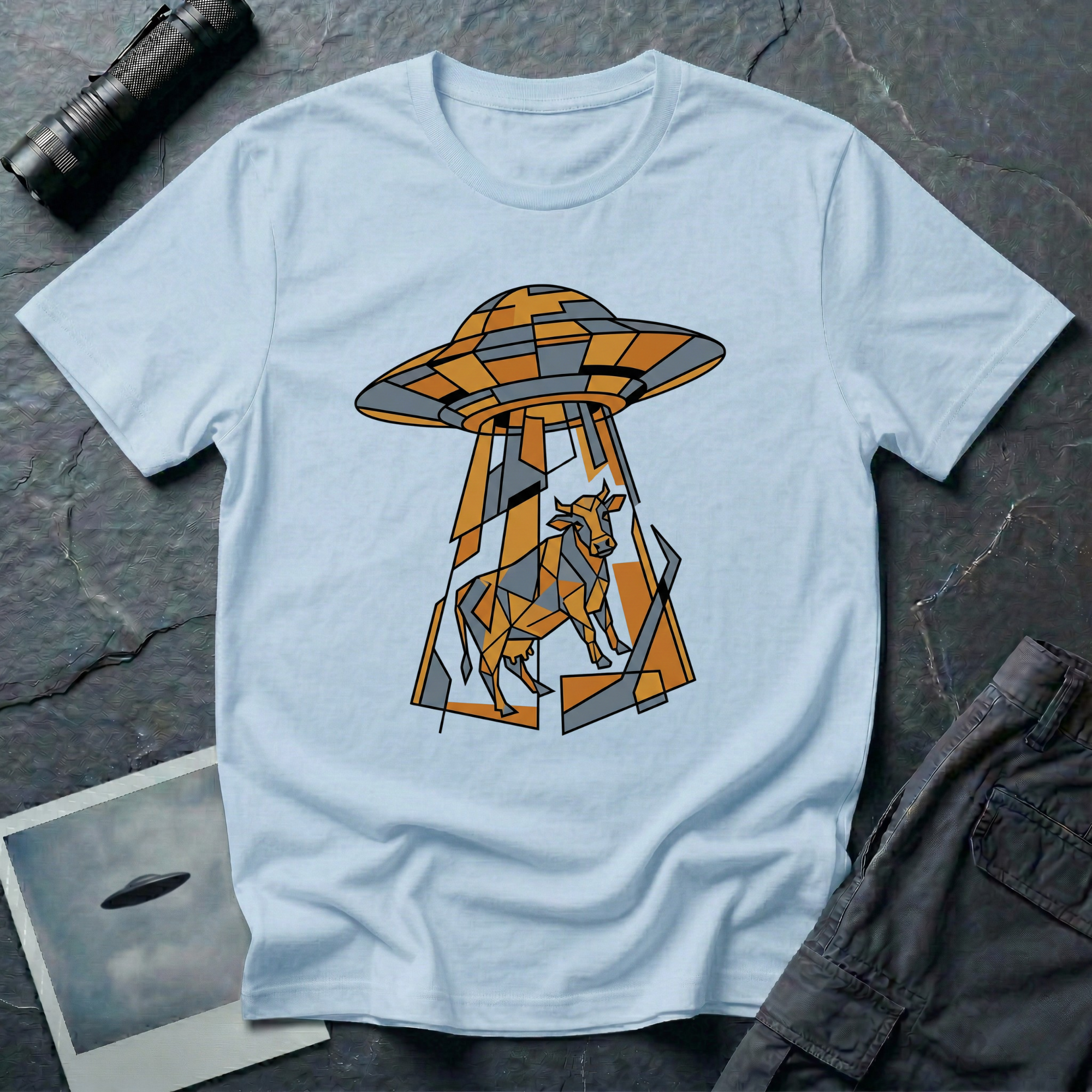 Cubist Cow geometric cow abduction t-shirt — flying saucer and suspended cow rendered in angular faceted planes of orange, grey, and white triangular geometric fragments on light blue cotton tee