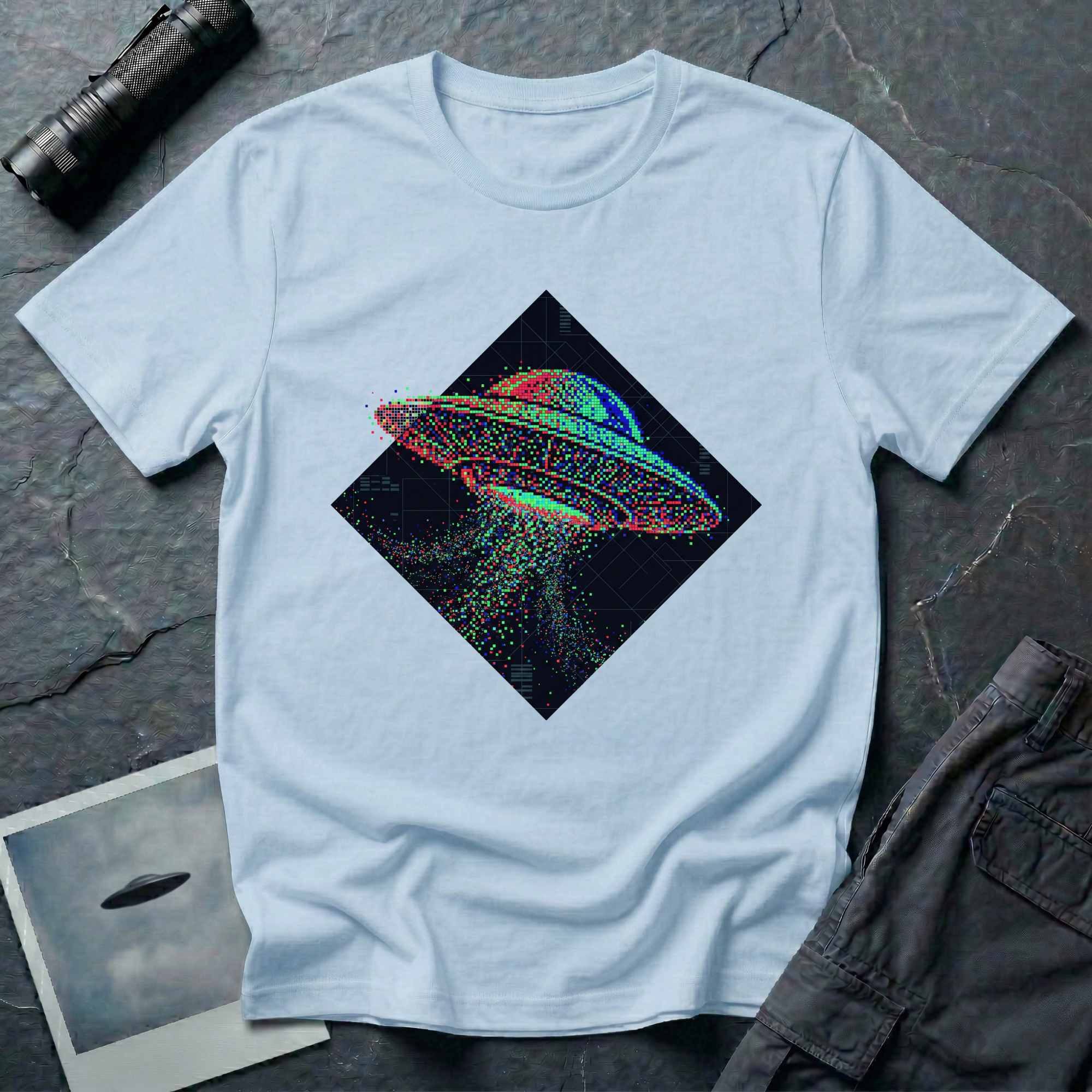 Glitch UFO t-shirt — flying saucer rendered in RGB pixel dots disintegrating inside a dark diamond frame on pale blue cotton tee