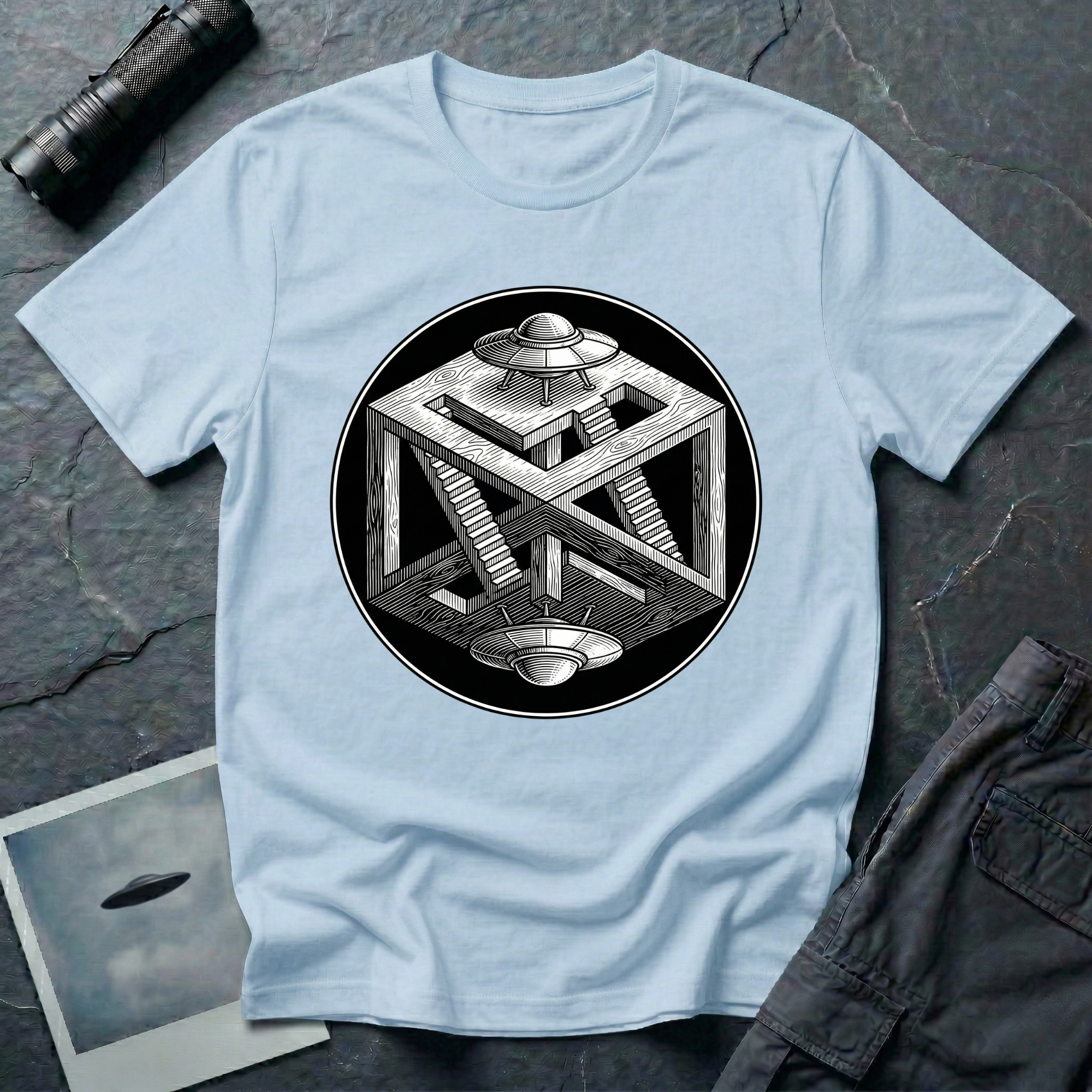 Escher UFO impossible geometry t-shirt — wood-engraved impossible cube with paradoxical staircases and two mirrored flying saucers inside a circular black medallion on light blue cotton tee
