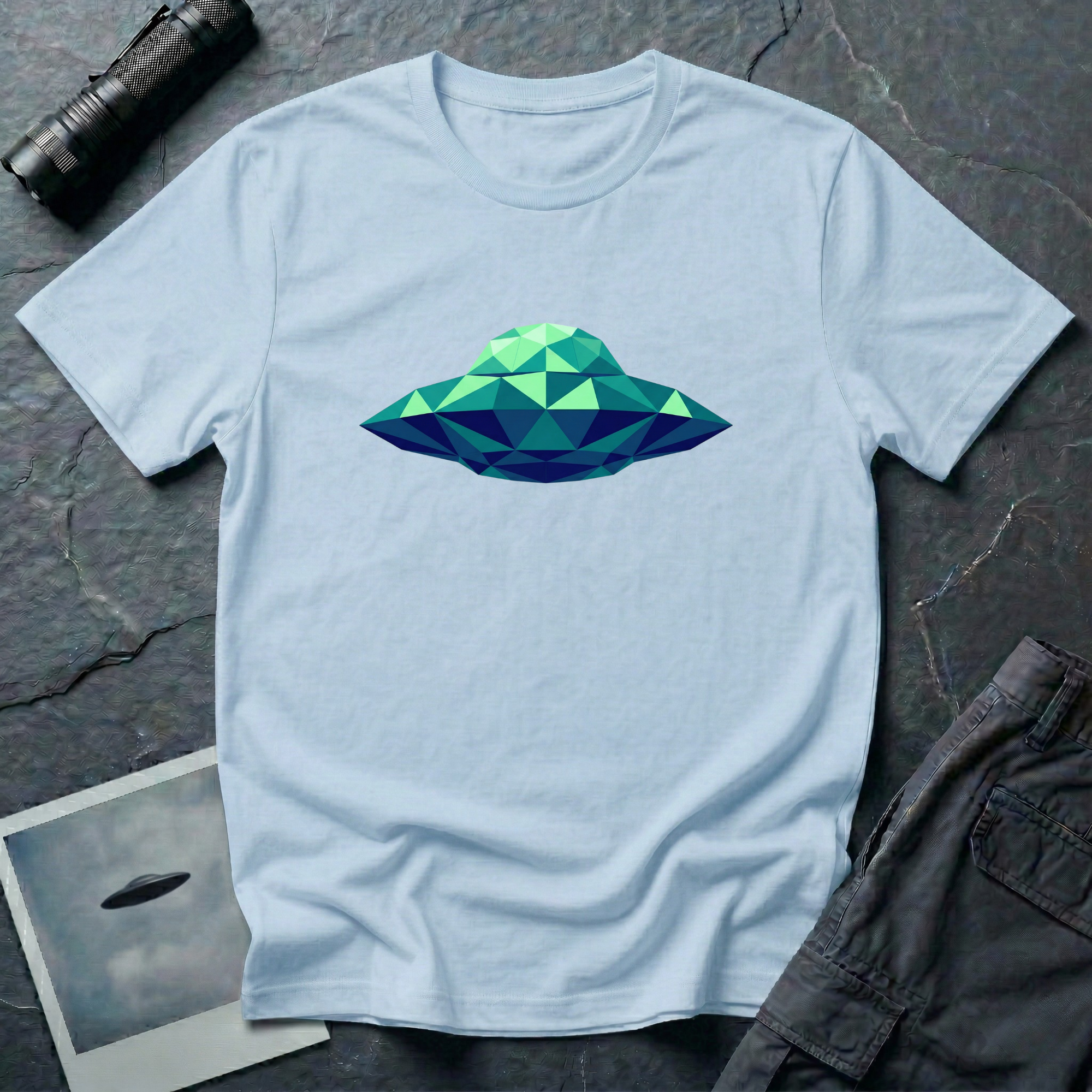 Cubist UFO geometric low poly t-shirt — classic flying saucer rendered in triangular facets of mint green, teal, and navy blue on light blue cotton tee