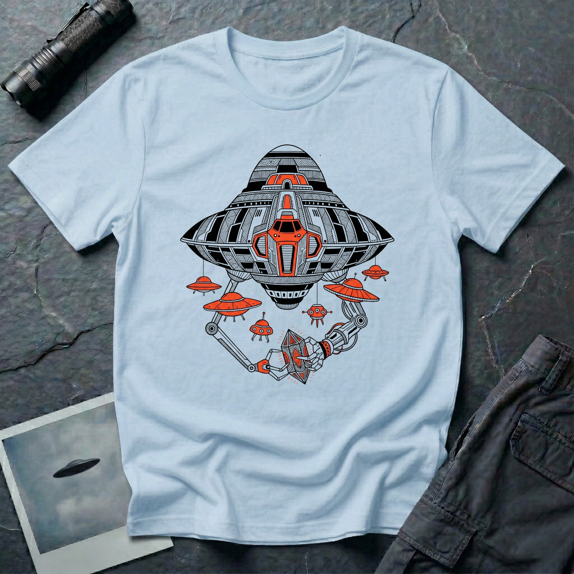 Light blue t-shirt with a black and orange mechanical UFO design featuring robotic arms holding an octahedral artefact and smaller saucer drones.
