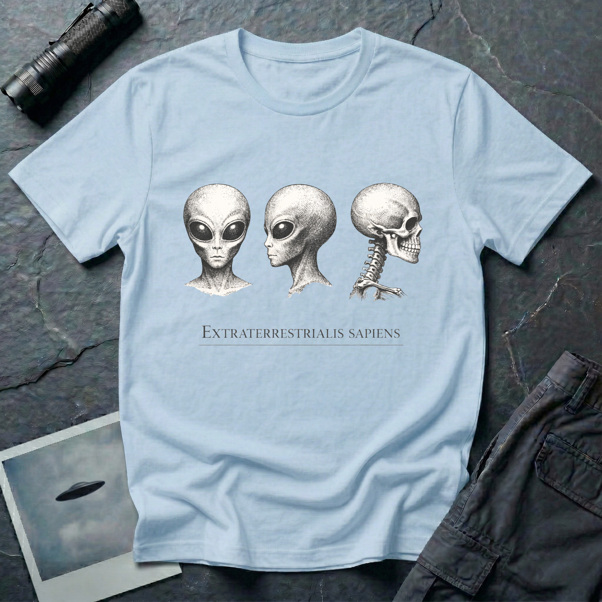 Extraterrestrialis Sapiens ancient aliens t-shirt — three heads in 19th-century anatomical study style with grey alien front and profile views and human skull on pale blue cotton tee