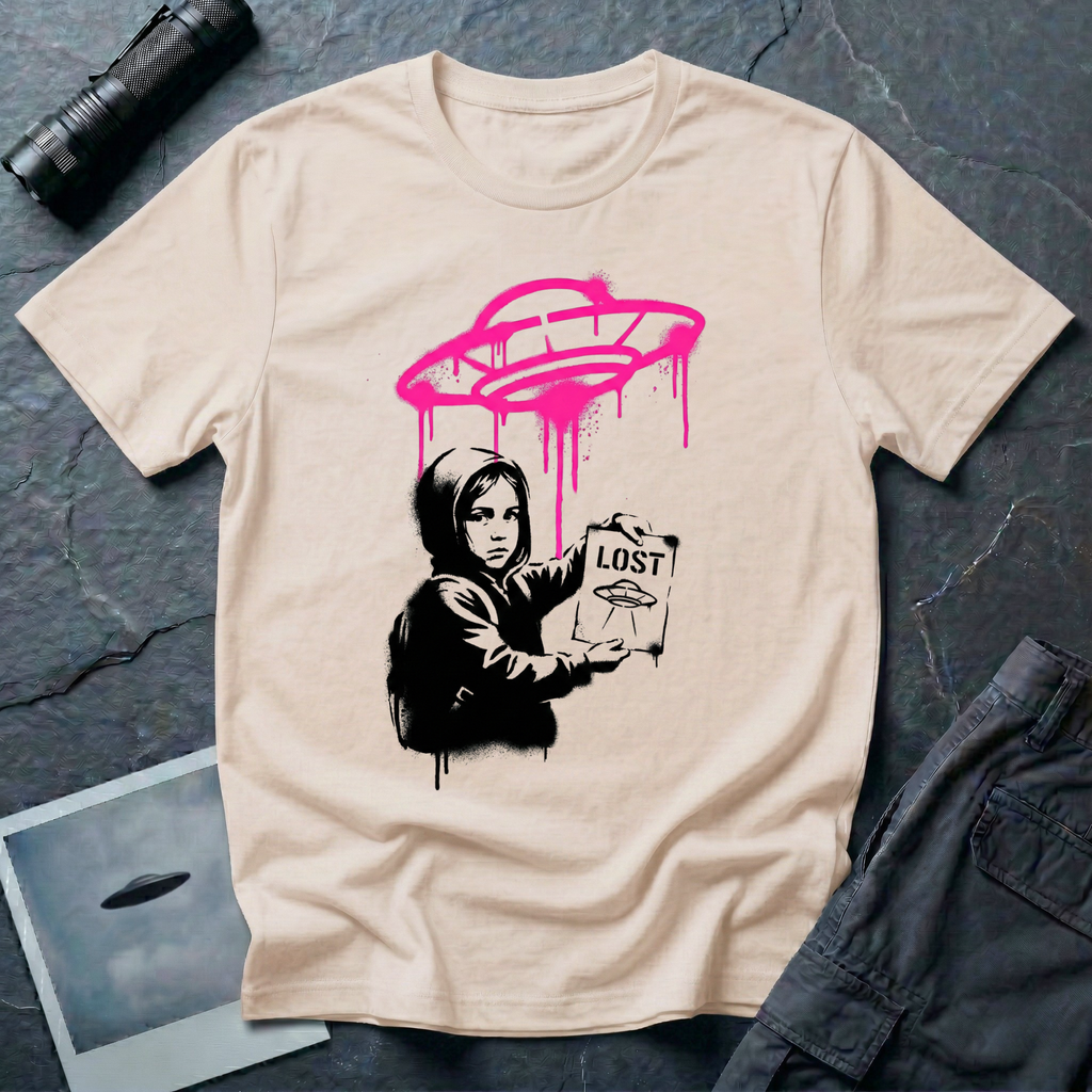 Street art UFO t-shirt with black stencil hooded figure holding "LOST" poster featuring flying saucer icon, bright magenta spray-painted UFO with paint drips hovering above in Banksy graffiti style on natural cotton tee