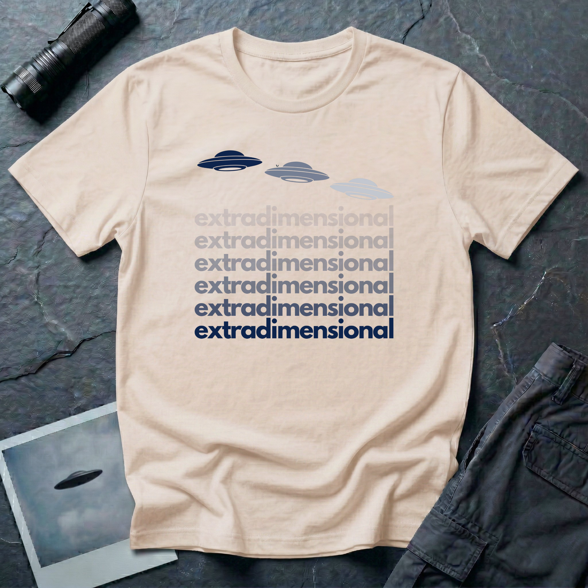 Natural t-shirt with three UFO saucer silhouettes in navy to grey gradient above the word extradimensional repeated six times in stacked bold type fading from grey to navy