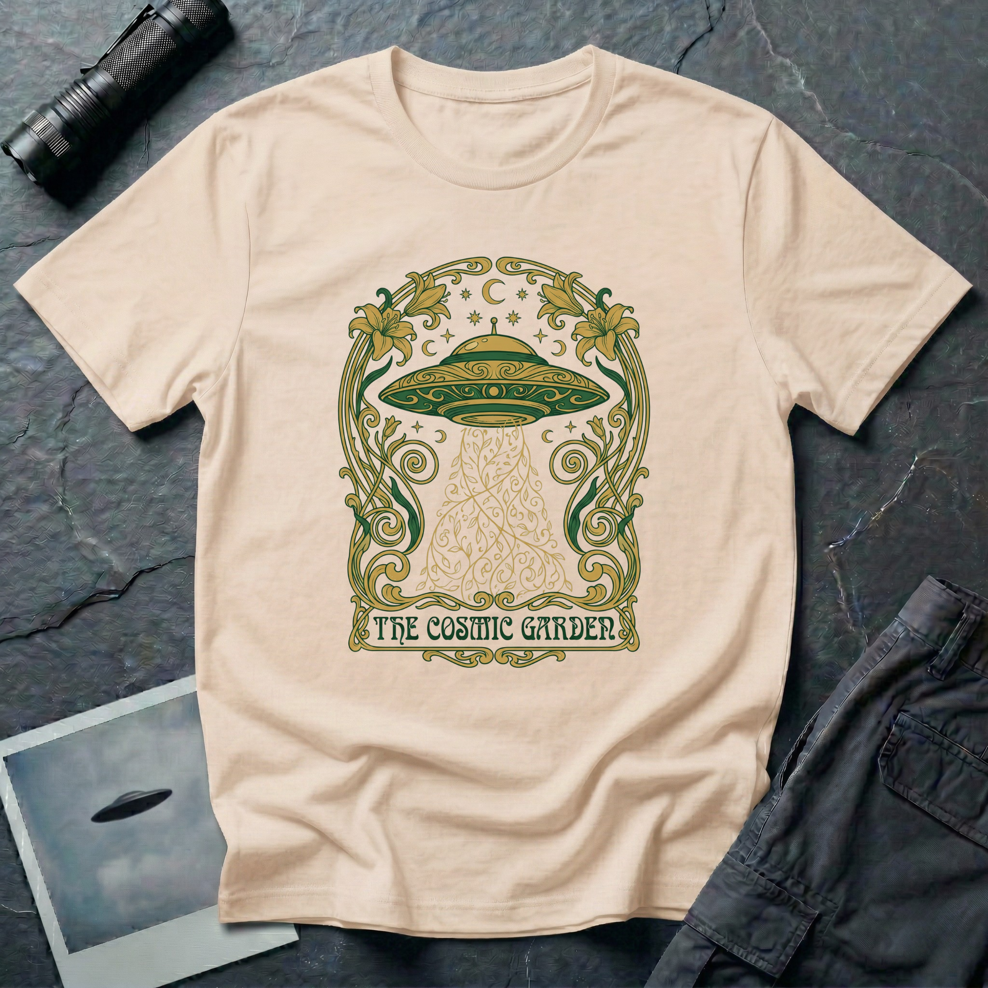 The Cosmic Garden Art Nouveau UFO t-shirt — ornate Mucha-style frame with flying saucer and botanical beam in green and gold on natural cotton tee