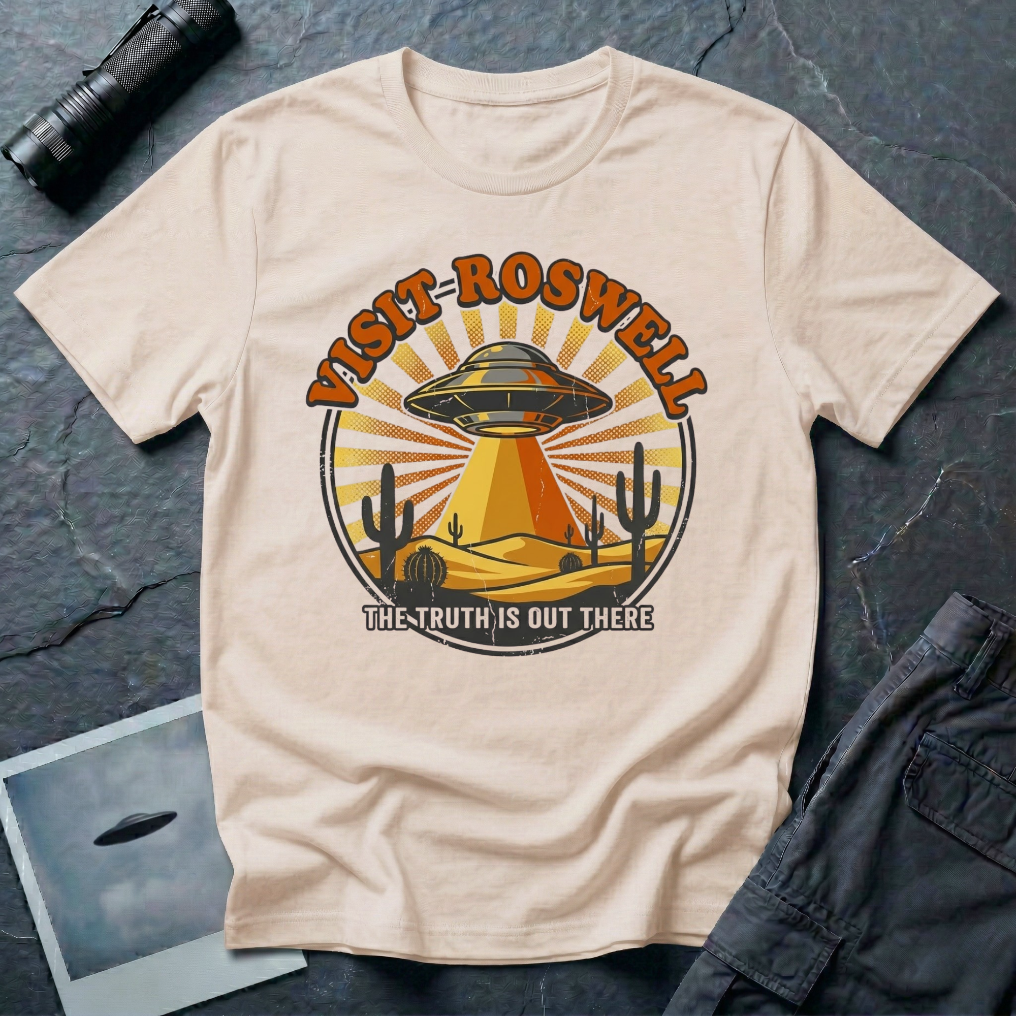 Visit Roswell UFO t-shirt — vintage circular tourism badge with flying saucer beaming over desert cacti in rust and mustard tones on natural cotton tee