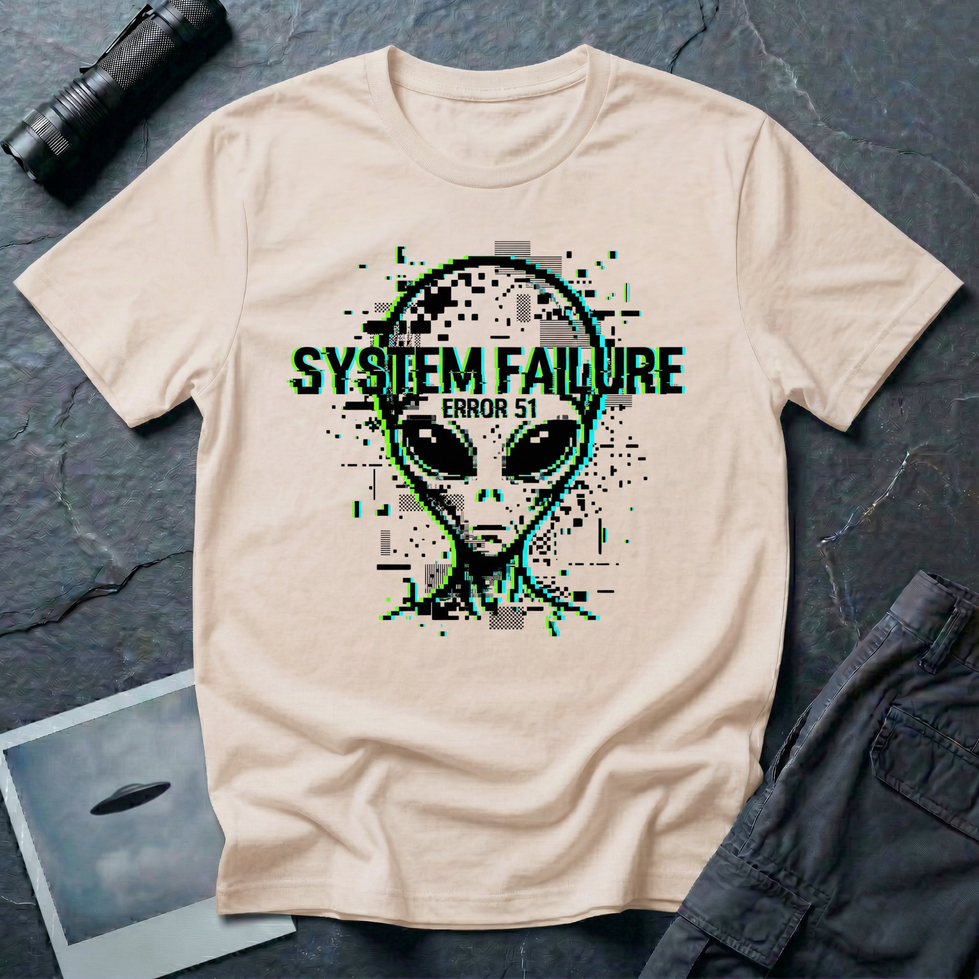 System Failure simulation UFO t-shirt — grey alien head fragmenting into pixel debris with chromatic glitch and "Error 51" on beige cotton tee