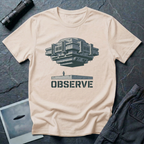 Observe Brutalist UFO t-shirt — massive concrete architectural craft hovering over small figure on plinth with "Observe" stencil type on natural cotton tee