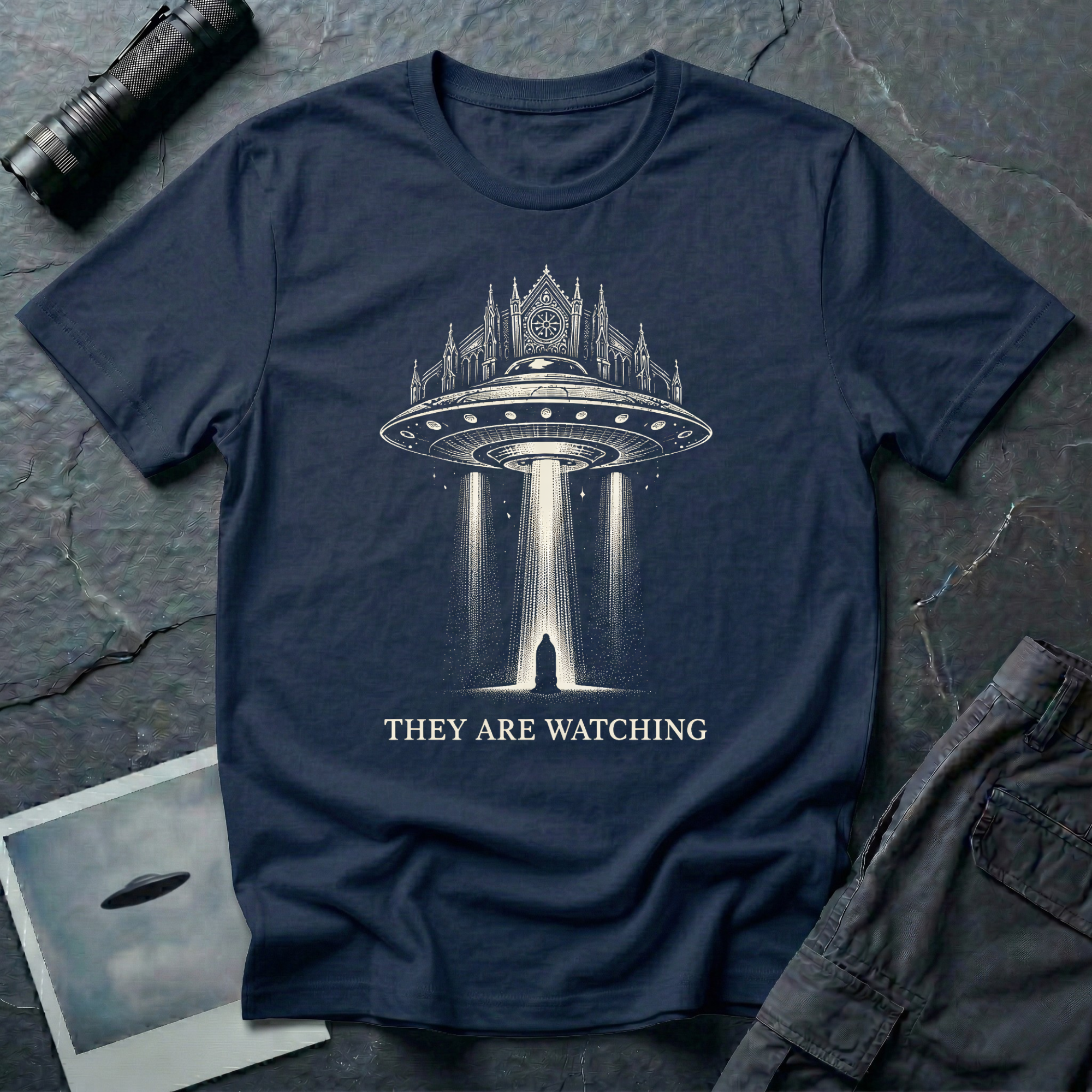 They Are Watching Gothic UFO t-shirt — medieval cathedral fused with flying saucer beaming down on hooded figure in cream line-work on navy cotton tee