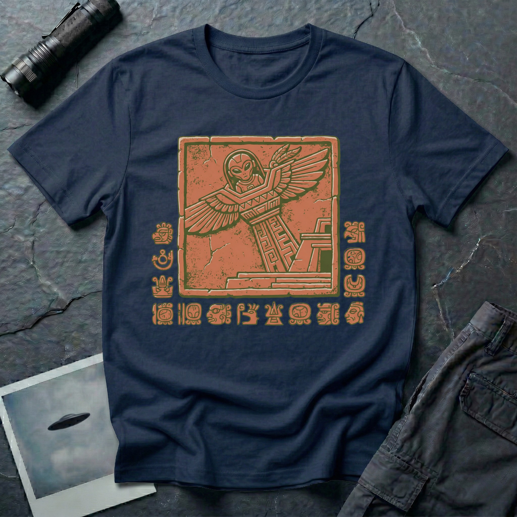 Aztec alien t-shirt — ancient astronaut figure with grey alien head in Mesoamerican feathered dress on stepped pyramid. Weathered stone relief on navy cotton tee.